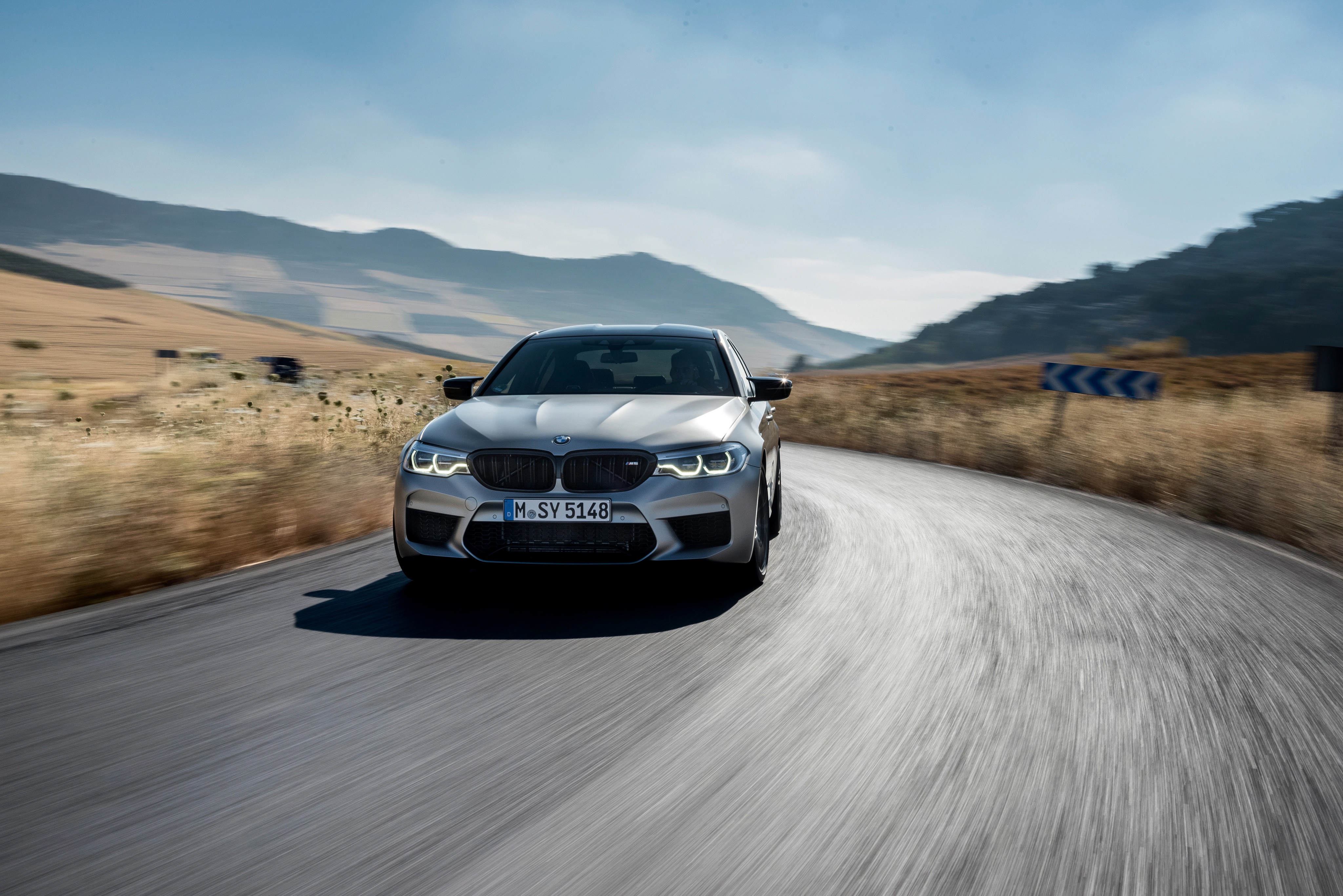 Silver BMW M5 Competition driving on a winding road HD Wallpaper