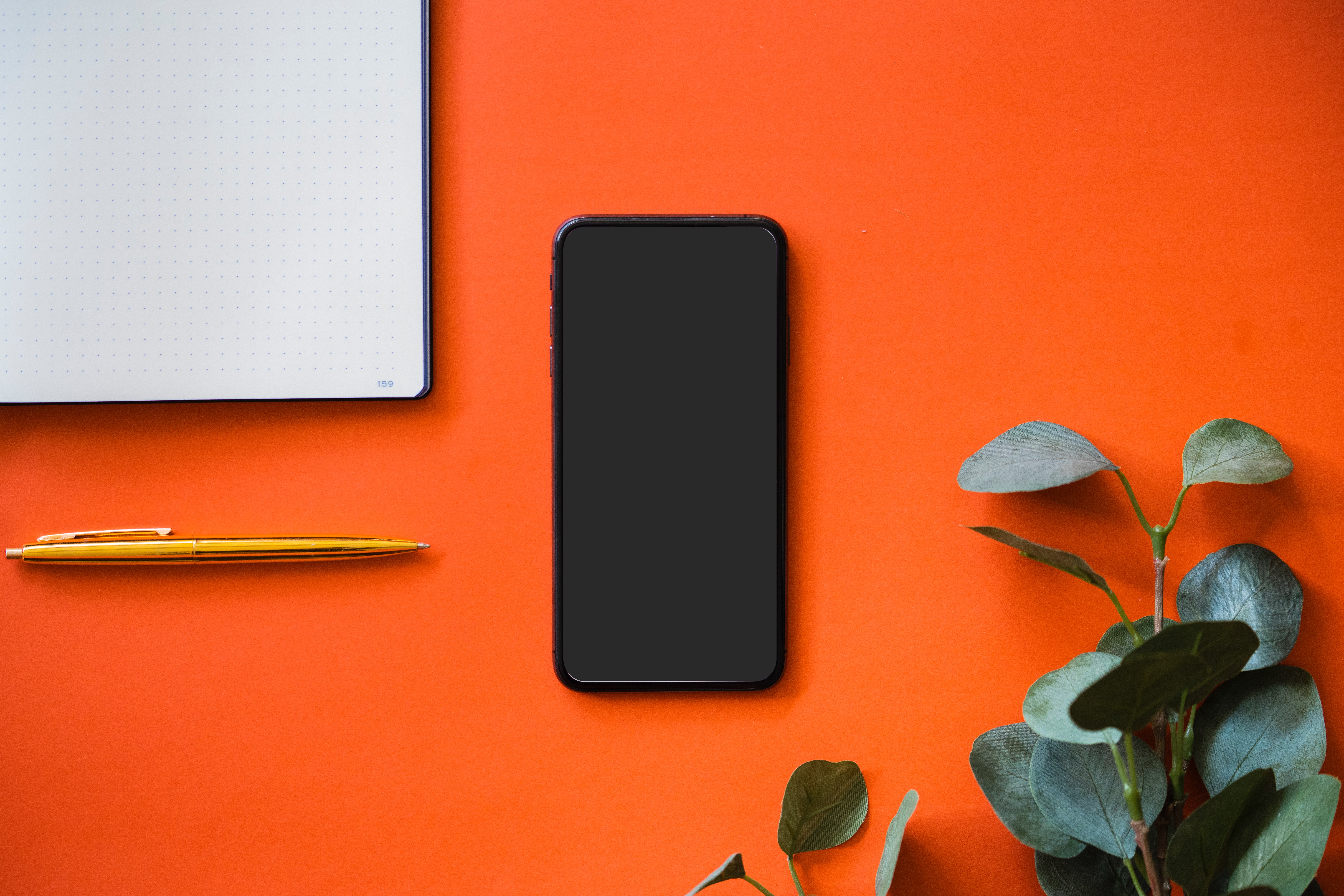 Black iPhone on an orange surface with a notebook and pen HD Wallpaper