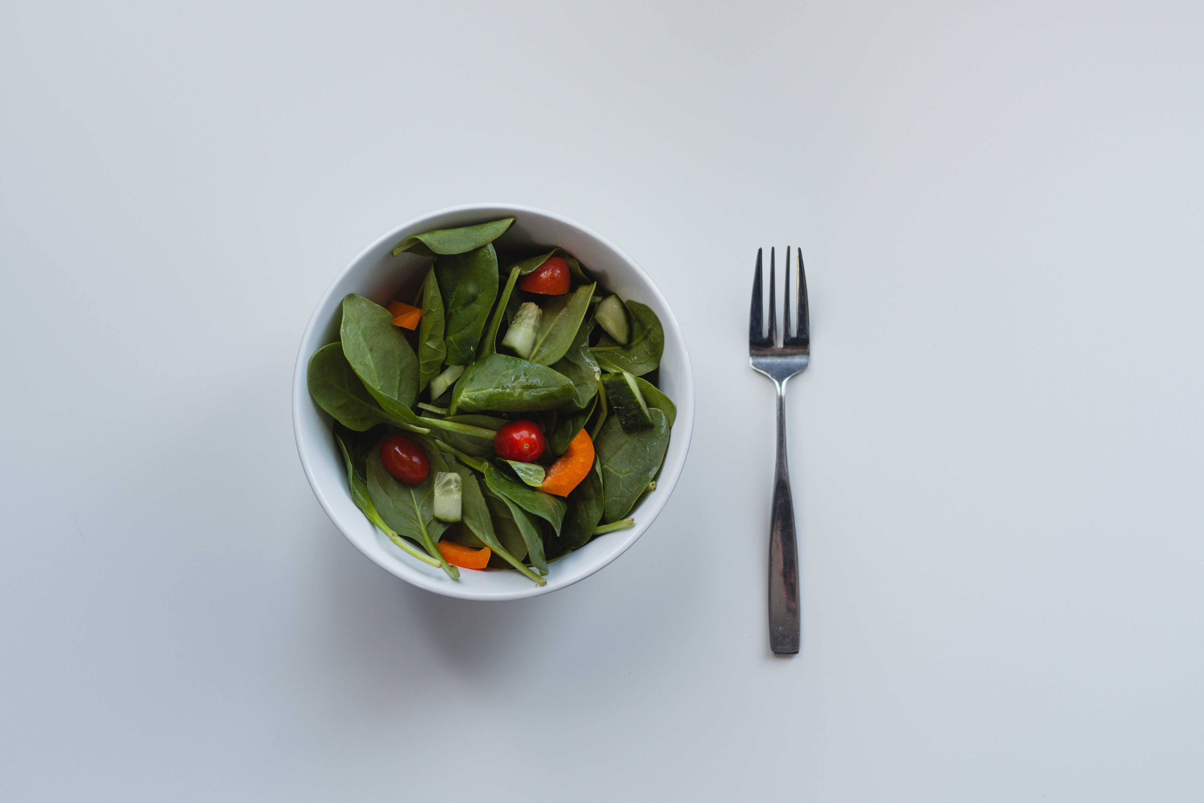A bowl of green salad with cherry tomatoes and cucumber next to a fork HD Wallpaper