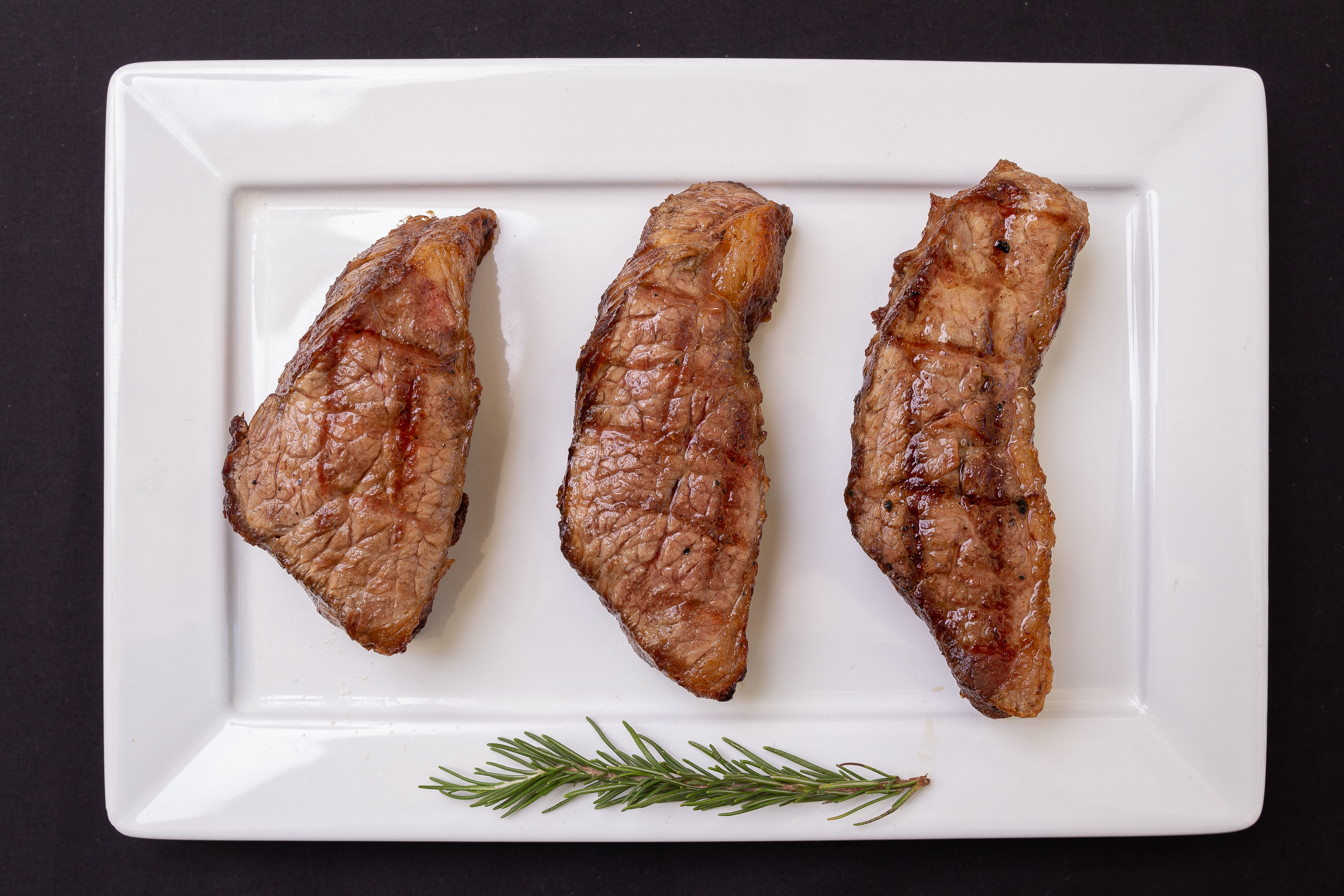 Three grilled steaks on a white plate with rosemary HD Wallpaper