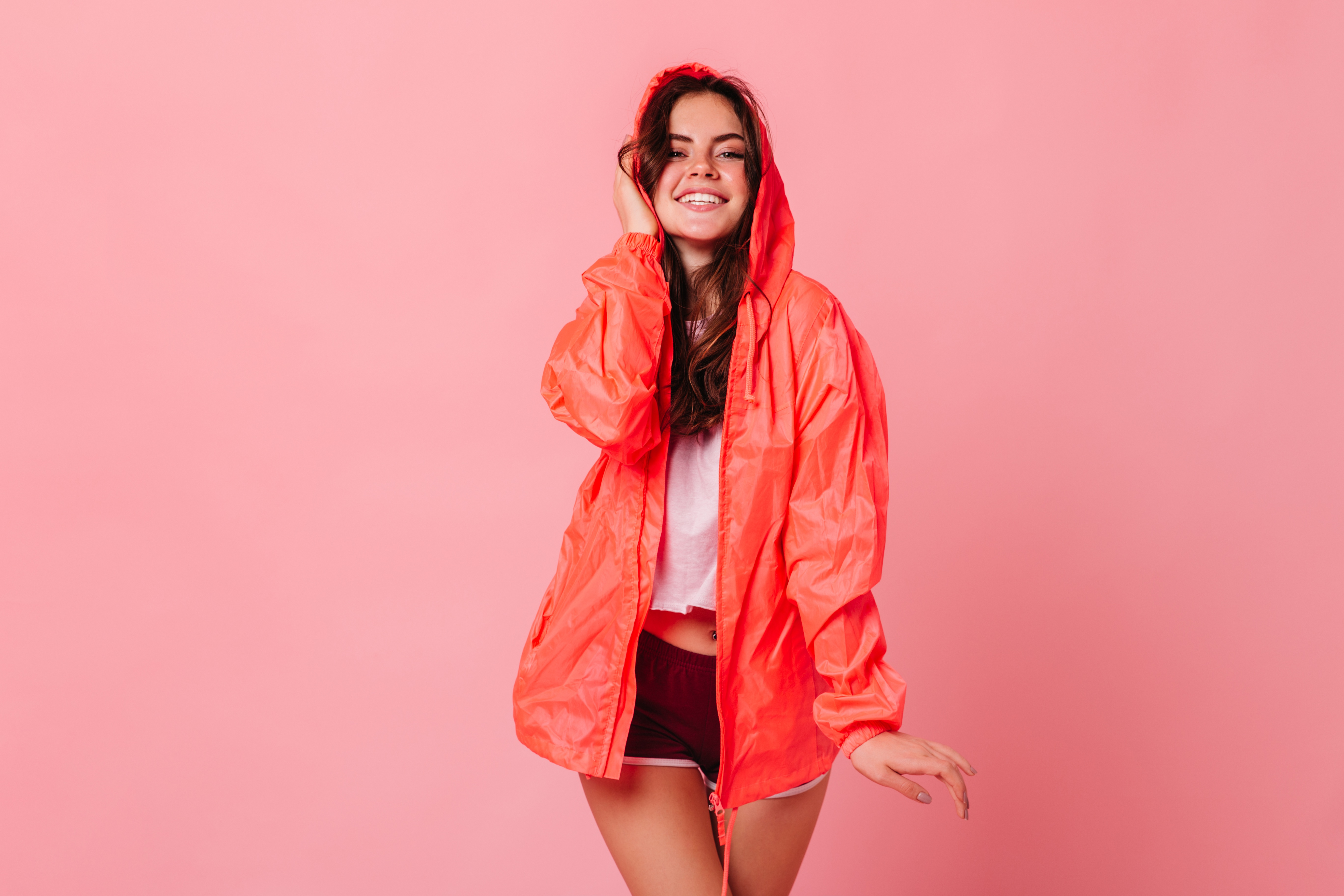 Woman in orange jacket and shorts smiling HD Wallpaper