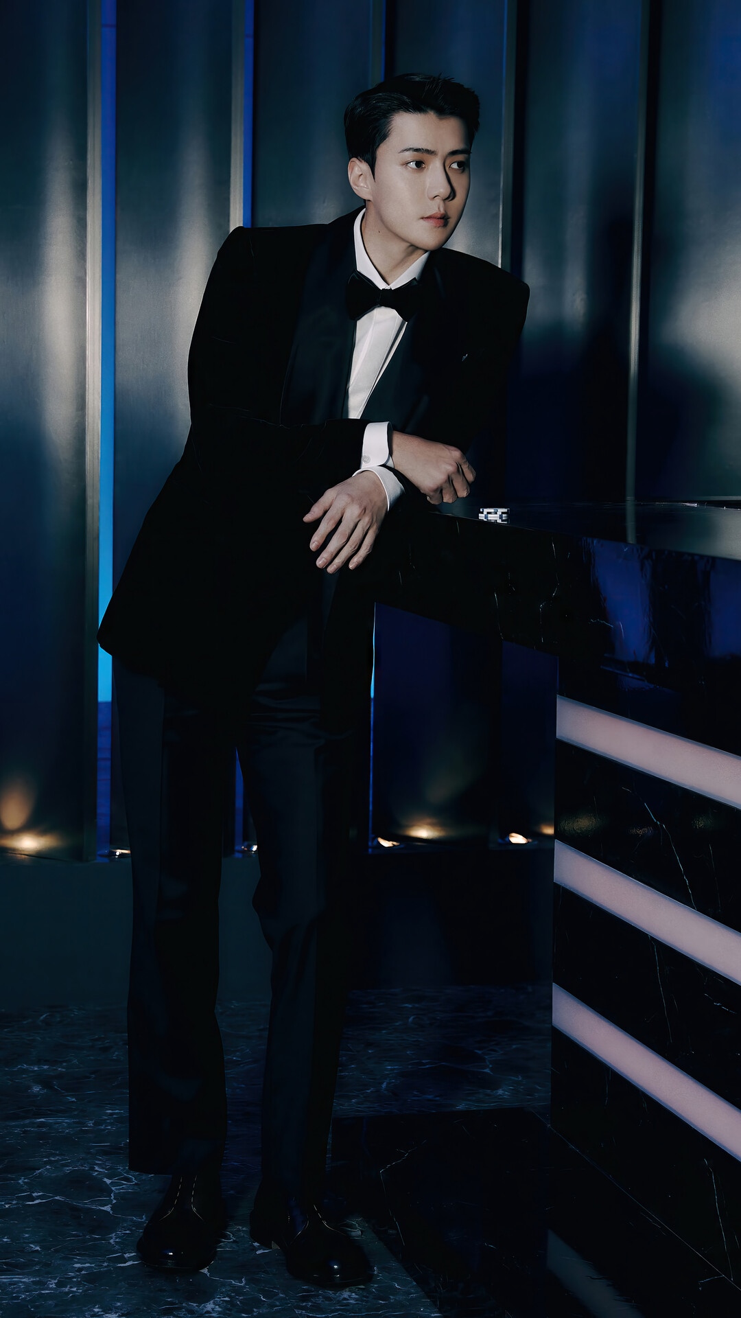 Sehun in a black tuxedo leaning on a counter HD Phone Wallpaper