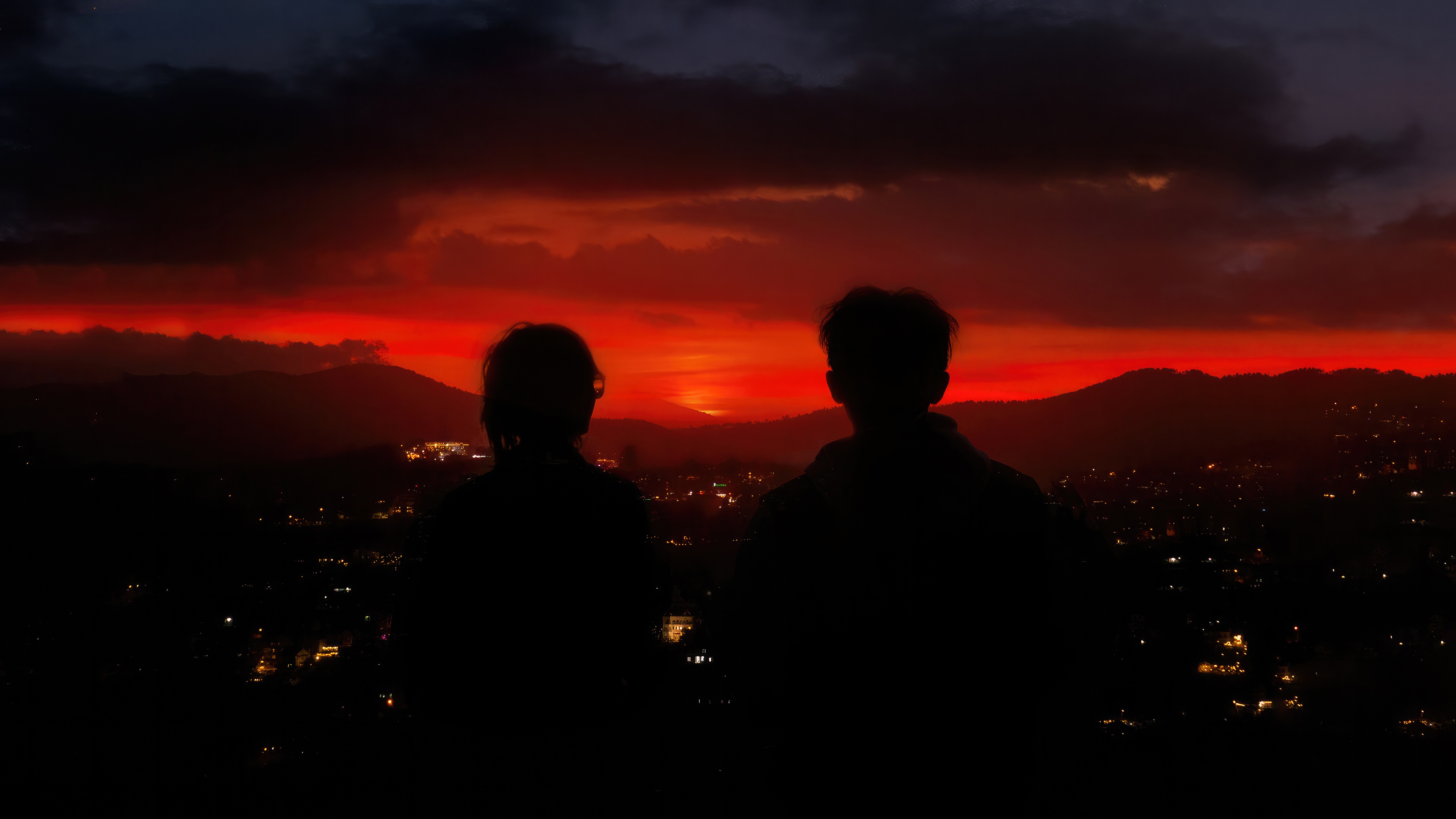 Couple watching a vibrant sunset over a city HD Wallpaper