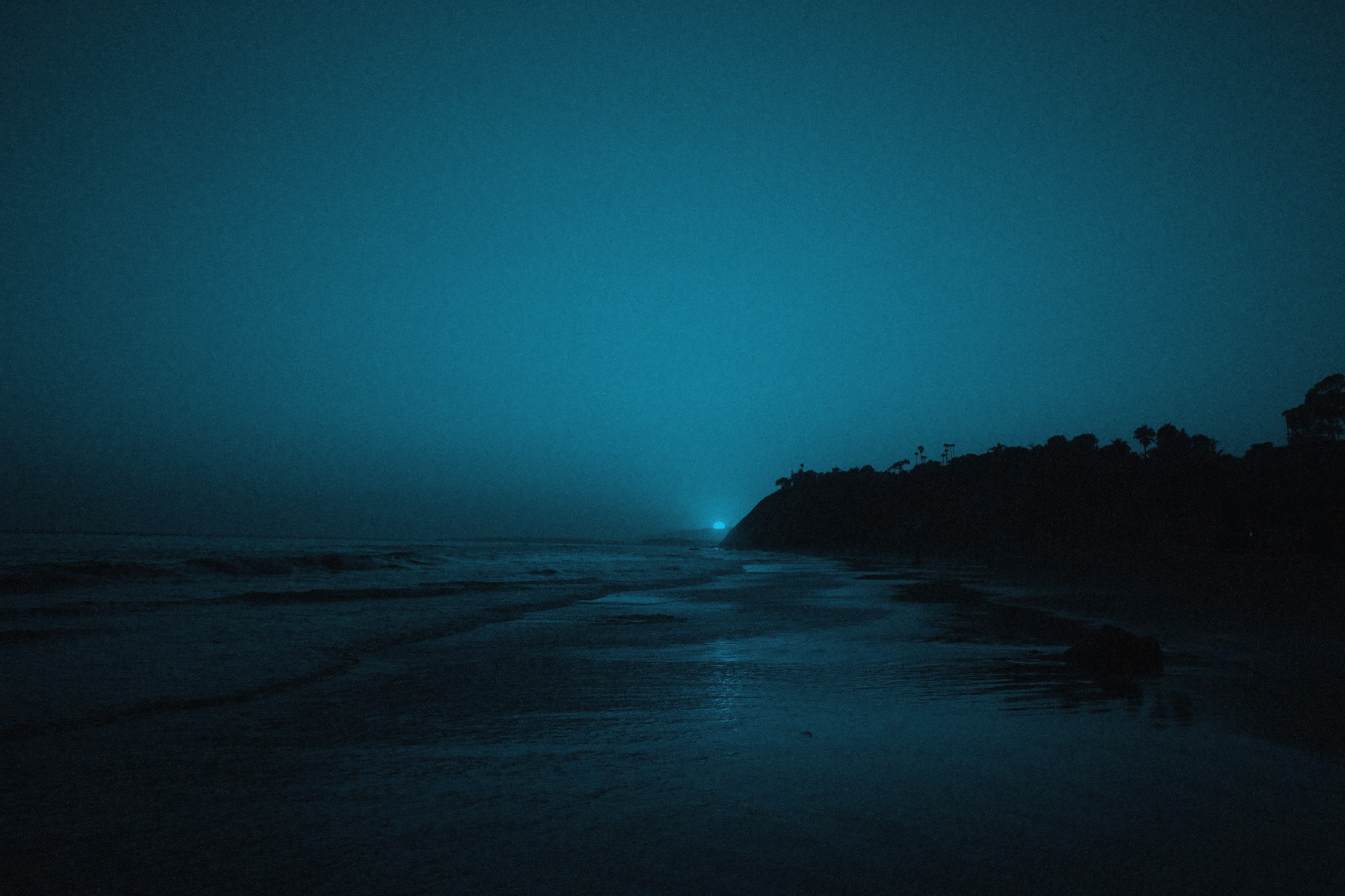 Ocean waves at dusk with a distant light on a hill HD Wallpaper