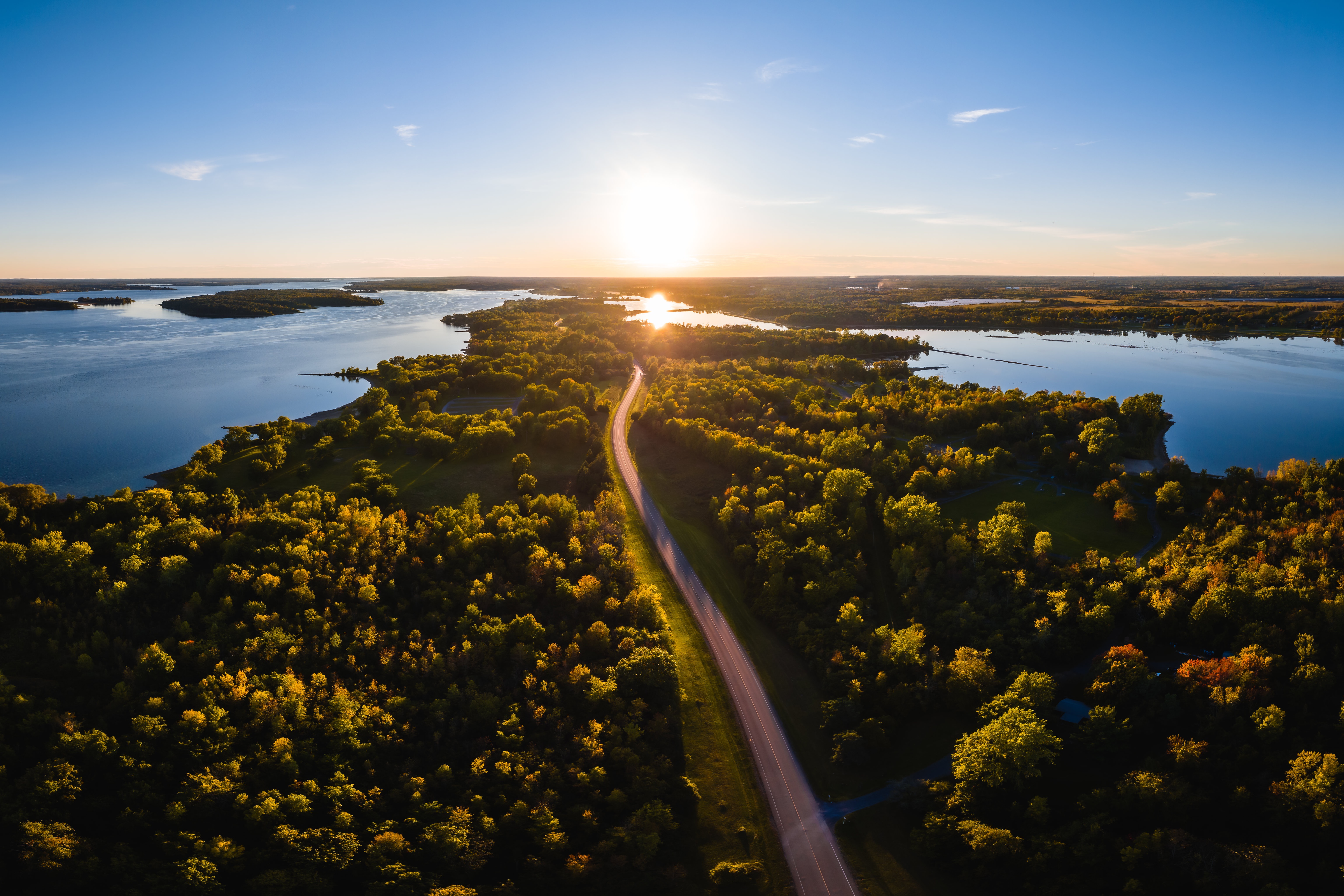 Aerial view of a road through a forest by a lake at sunset HD Wallpaper