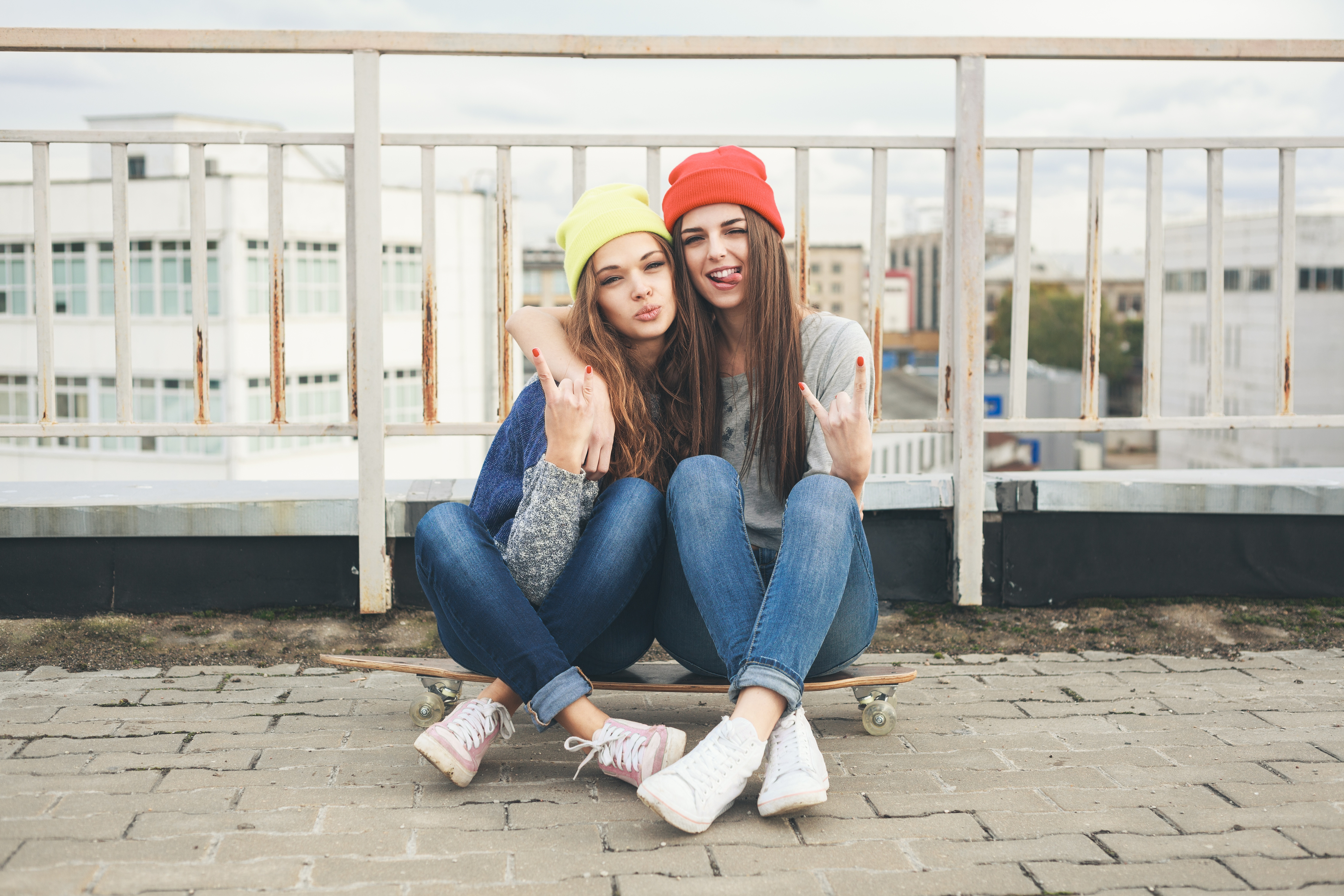 Two young women sitting on a skateboard HD Wallpaper