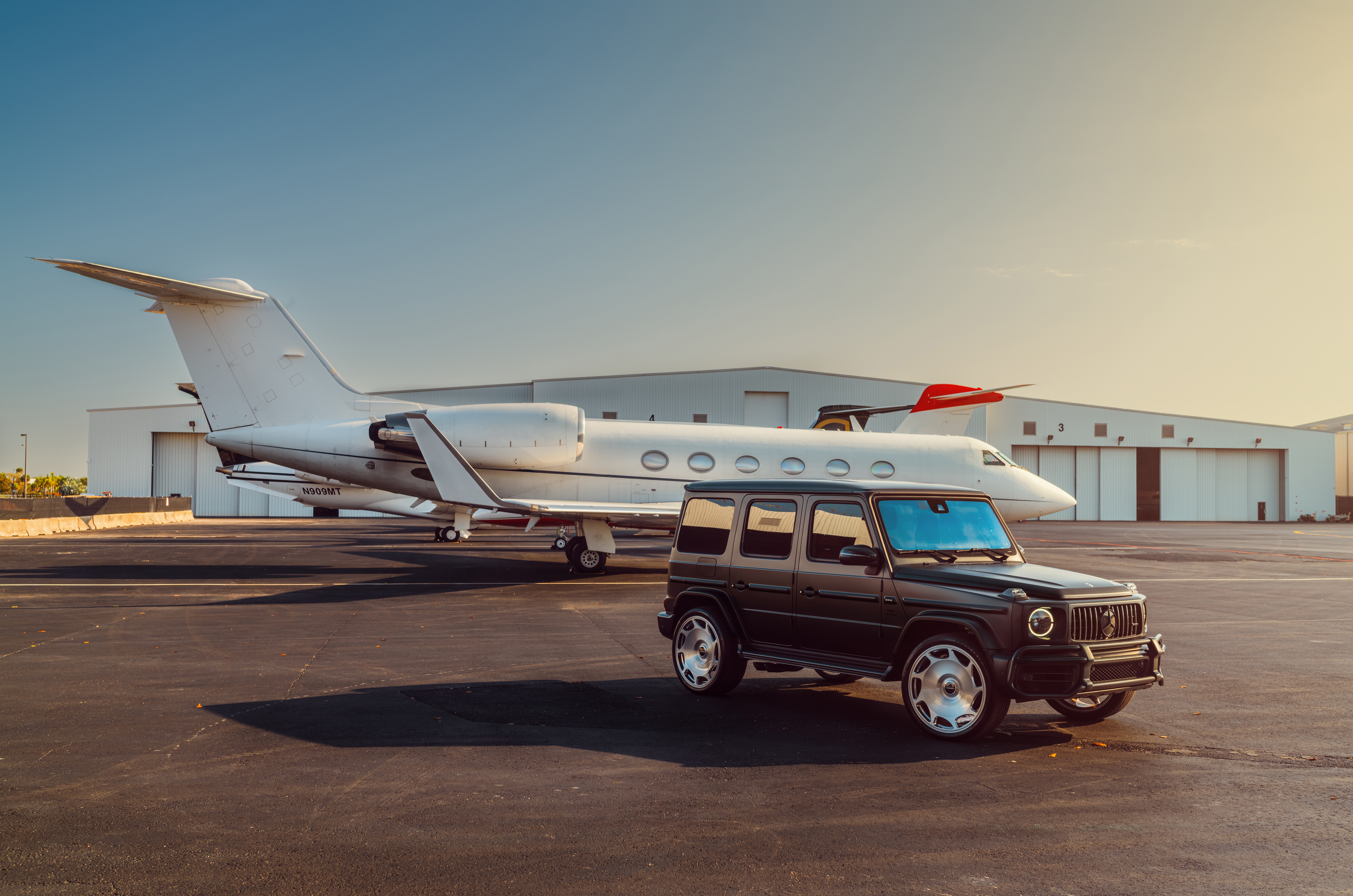 Mercedes G-Class parked by a private jet at an airport hangar HD Wallpaper