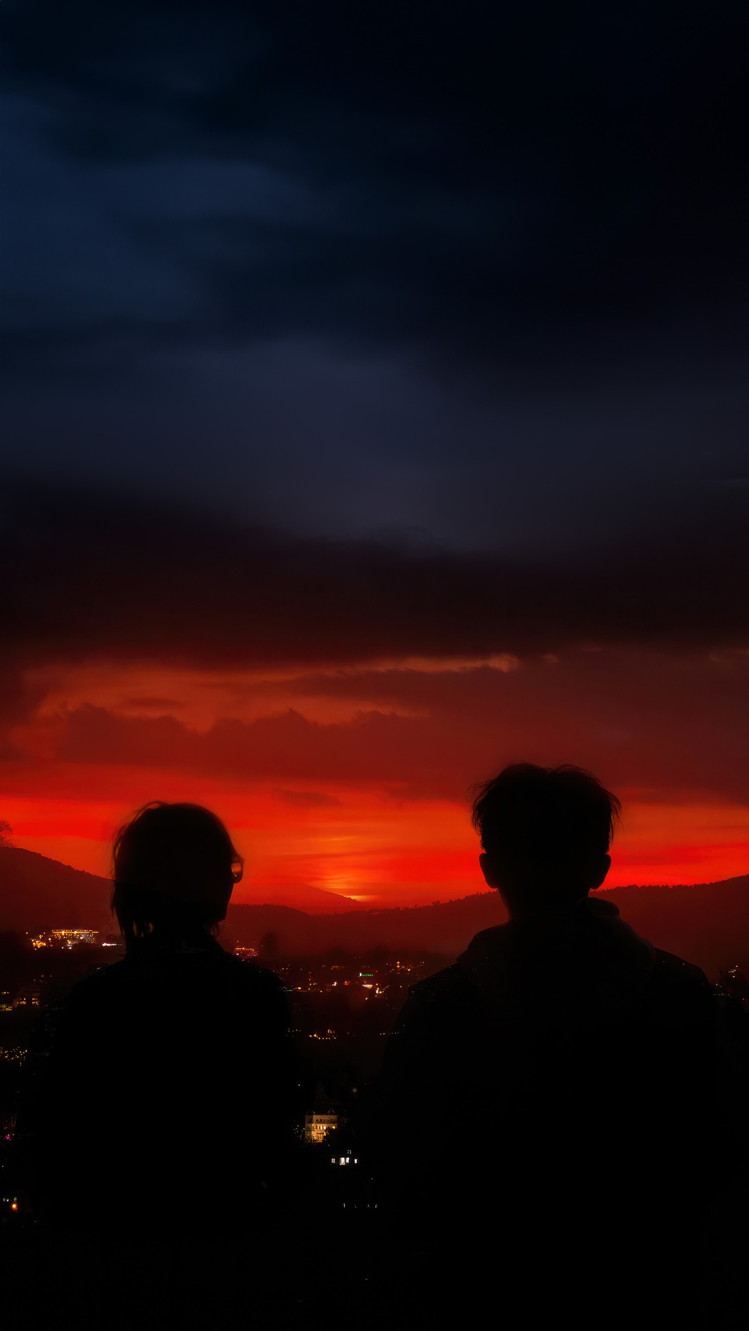 Couple watching a vibrant sunset over a city HD Phone Wallpaper