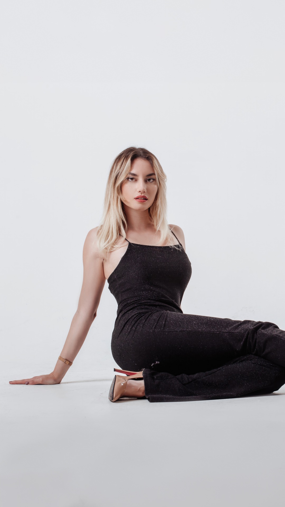 Model in a black dress sitting on a white background HD Phone Wallpaper
