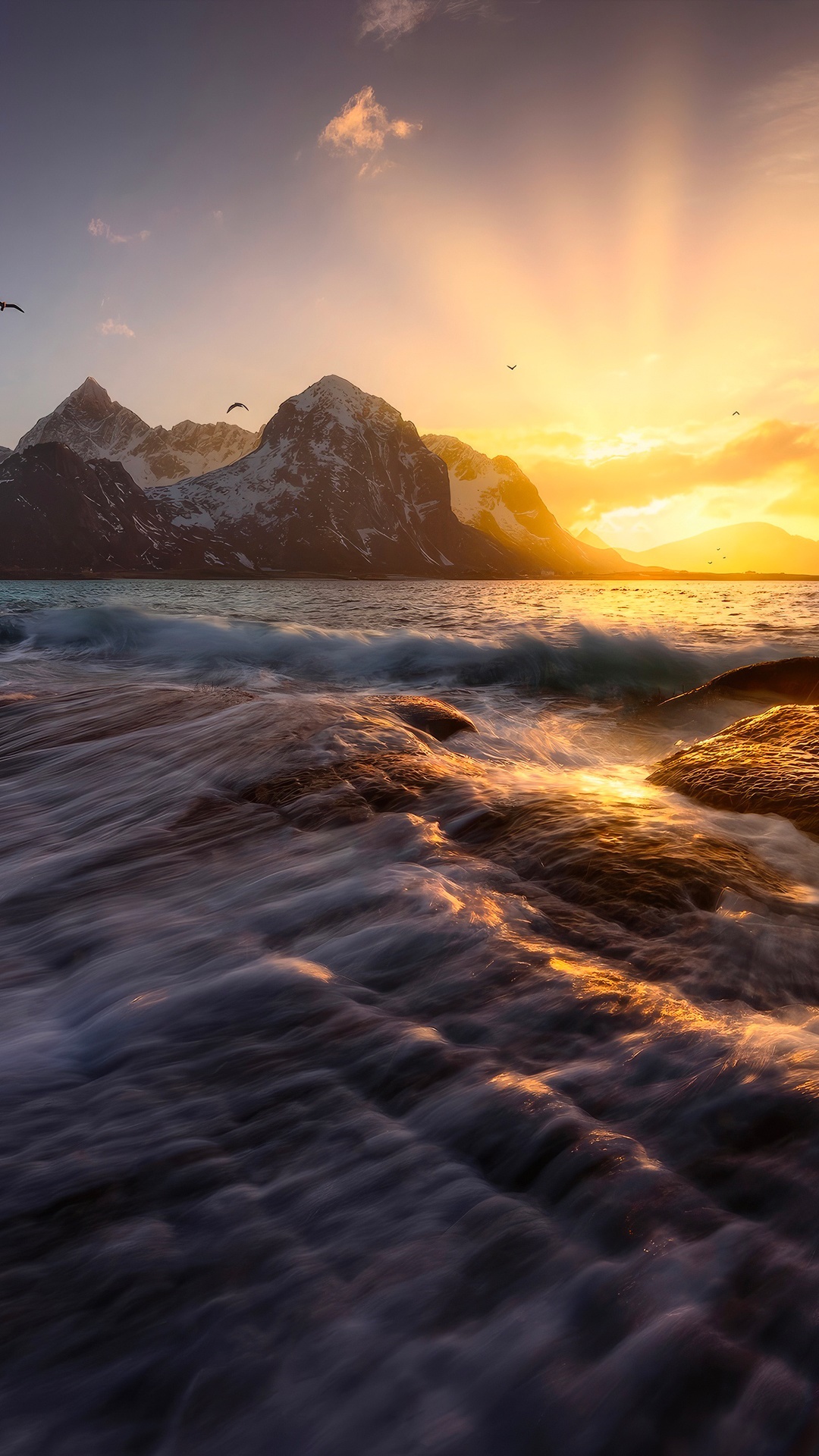 Waves crashing on rocks with snow-capped mountains at sunset HD Phone Wallpaper