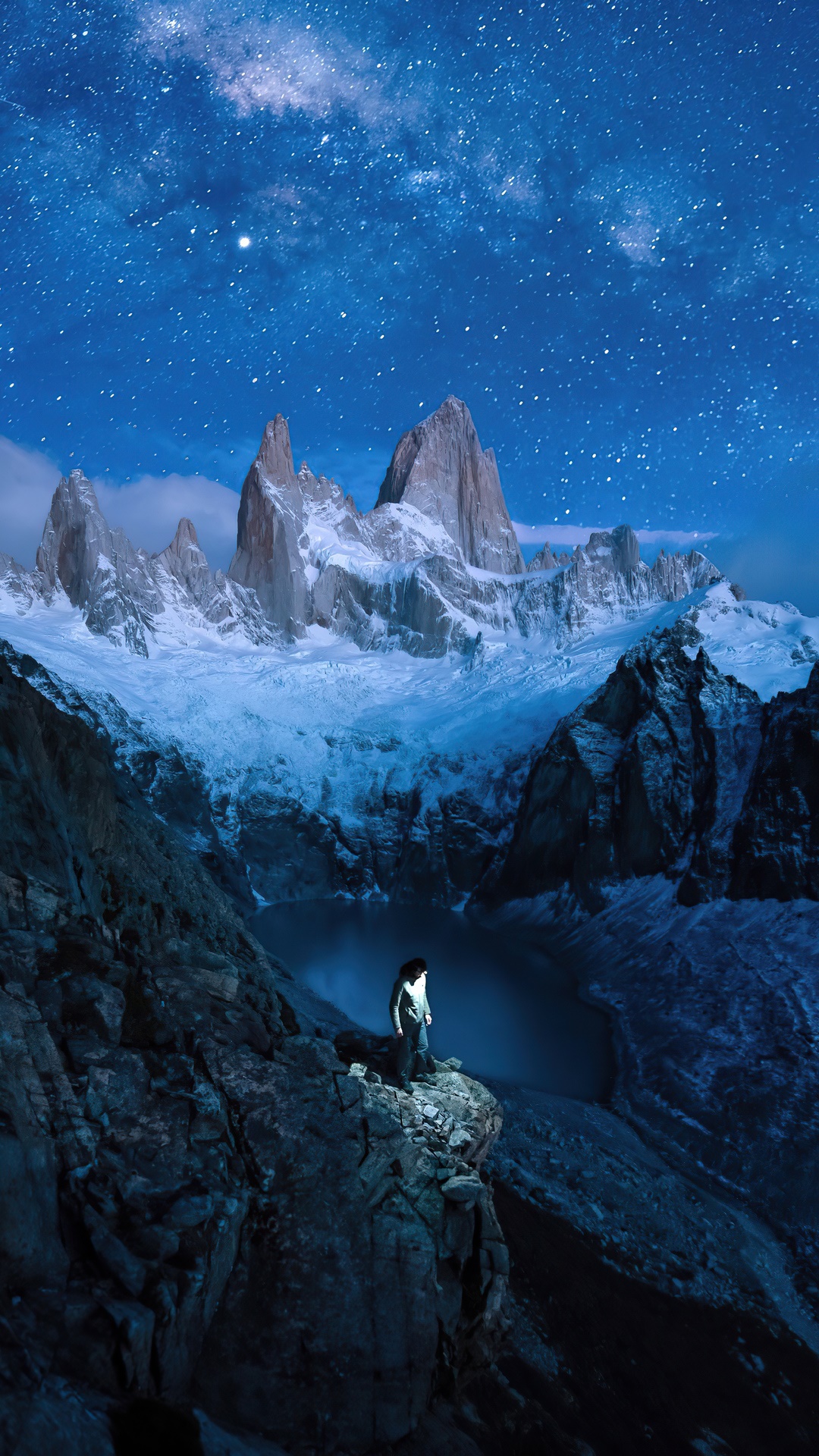 Person standing on a cliff under the starry sky with mountains HD Phone Wallpaper