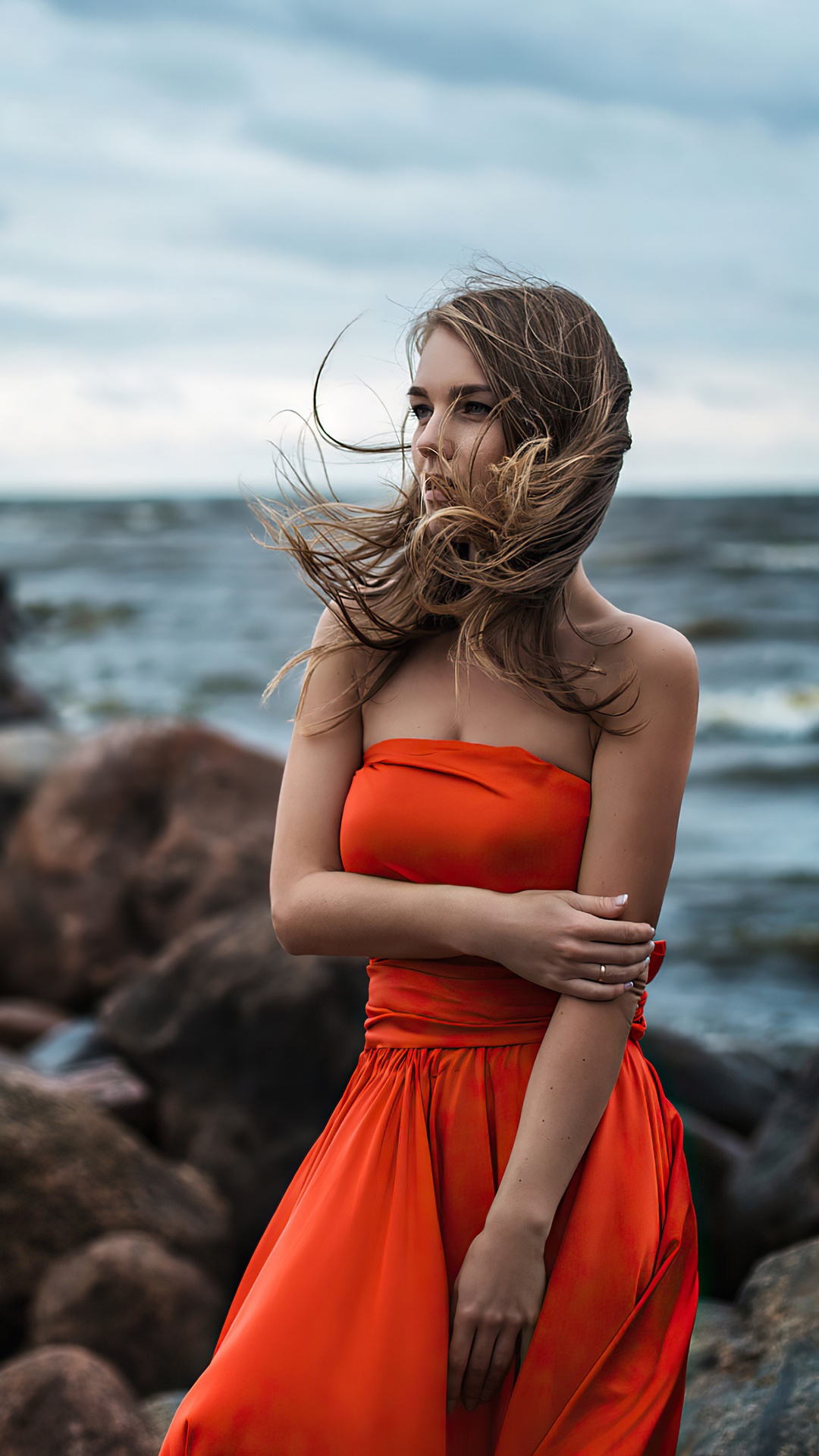 Woman in orange dress on rocky shore HD Phone Wallpaper