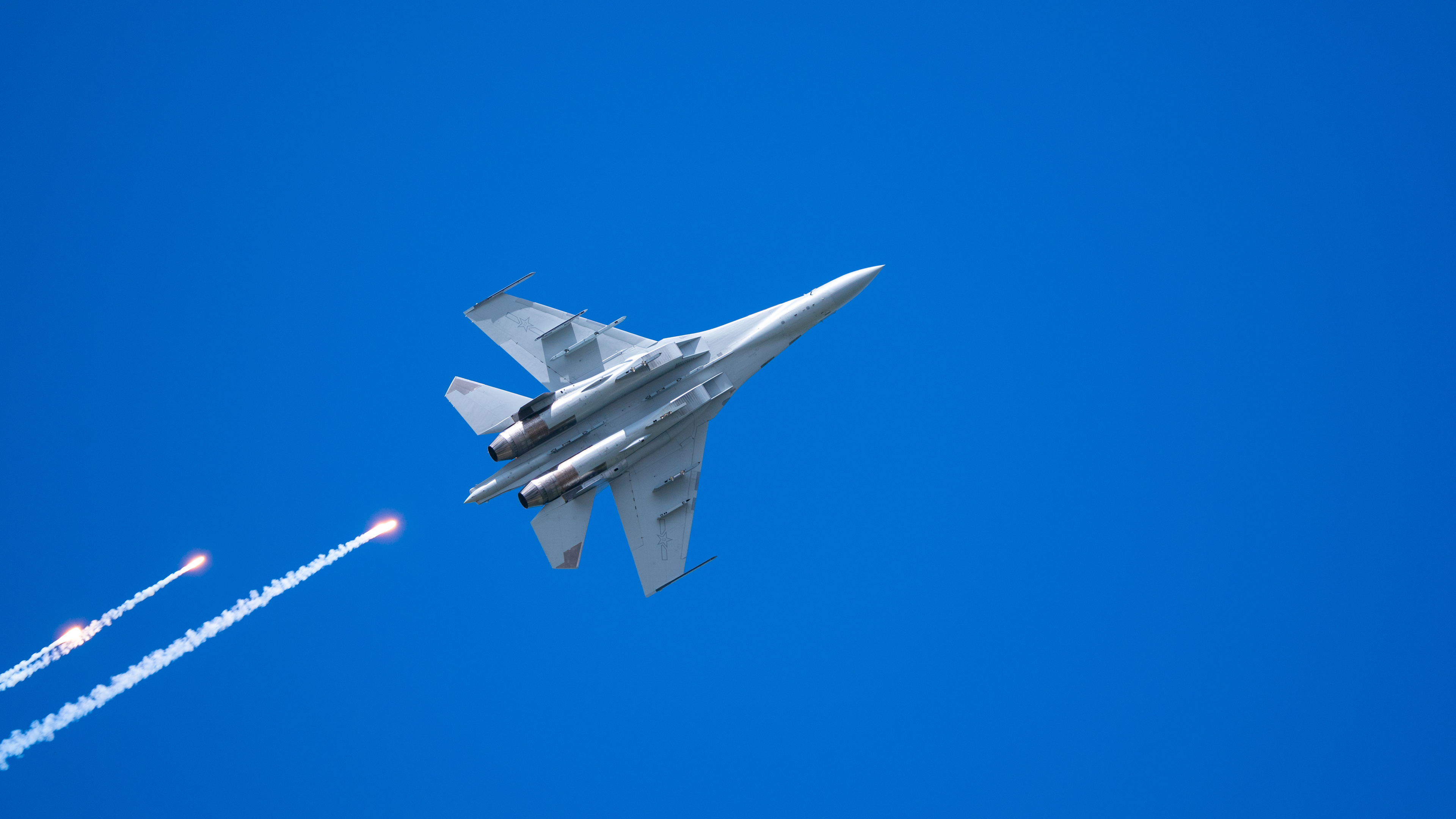 4K fighter jet firing flares against a blue sky HD Wallpaper