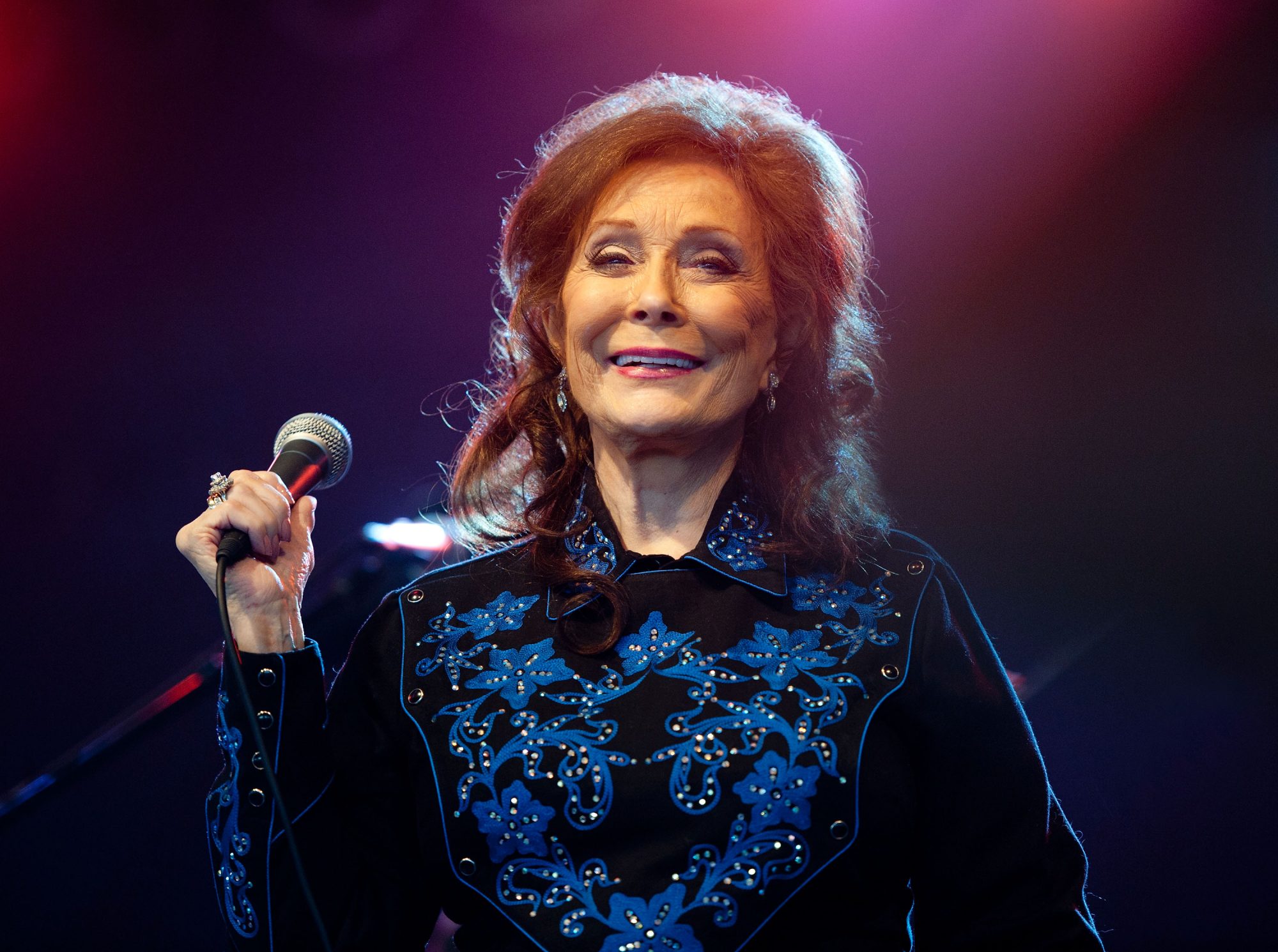 Loretta Lynn performs on stage with a microphone HD Wallpaper