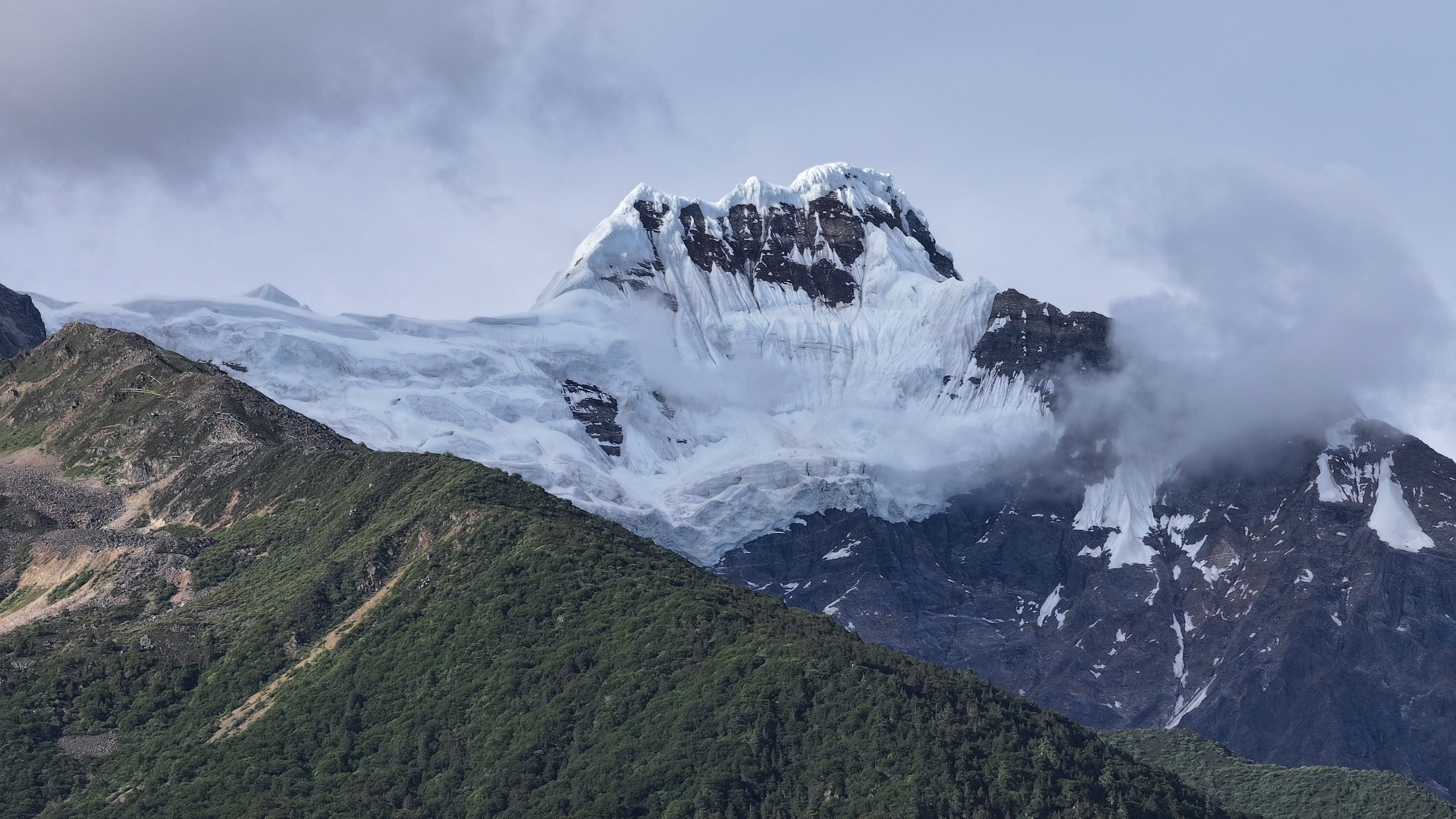 Snowy mountain peak with clouds and green slopes HD Wallpaper