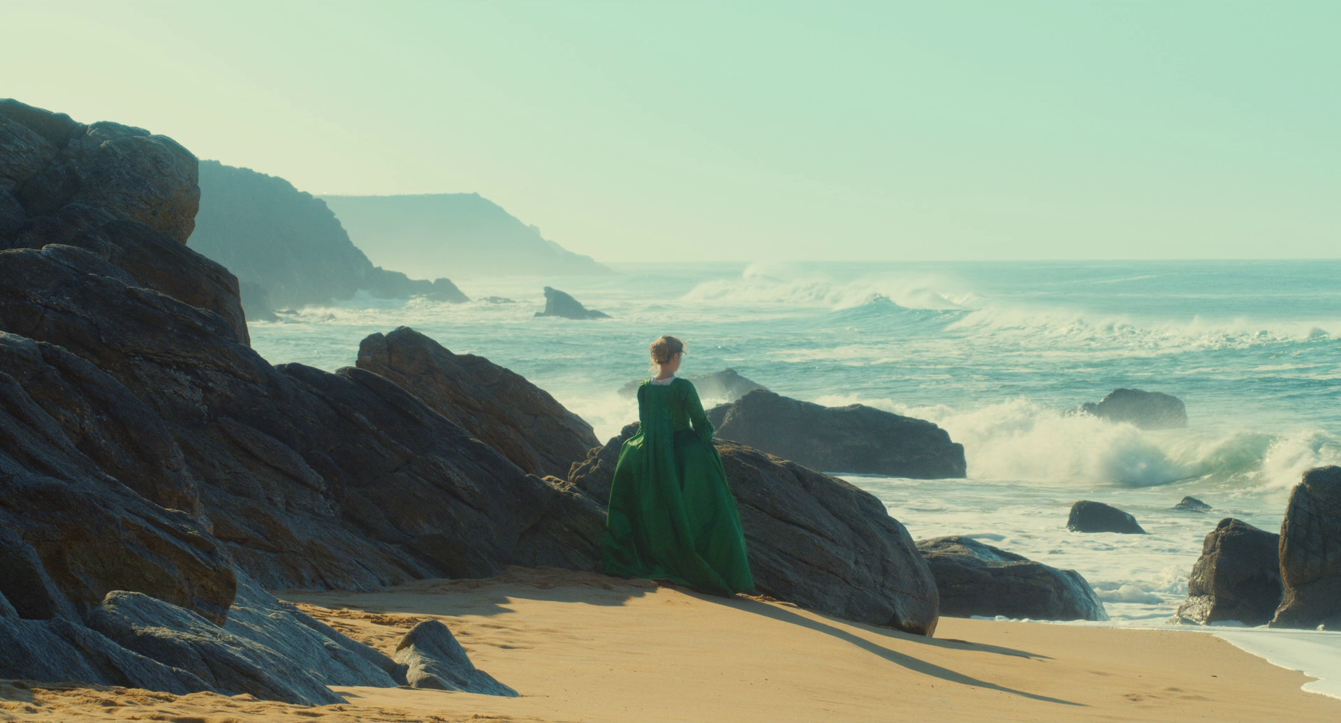 Woman in green dress on rocky beach with ocean waves HD Wallpaper