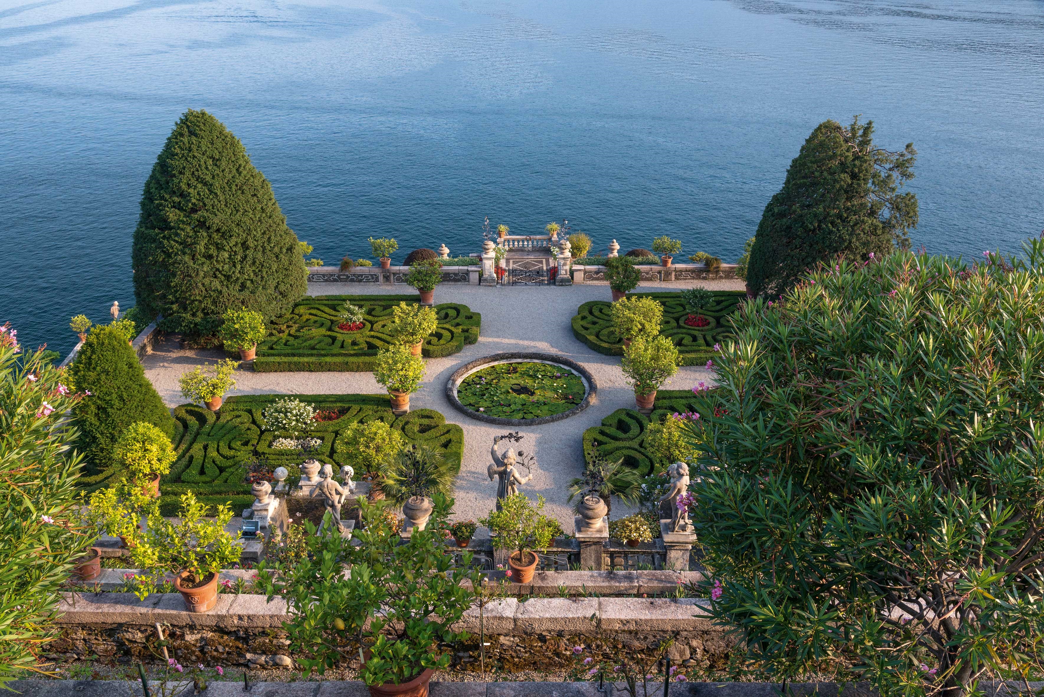 Italian garden with manicured hedges and a pond overlooking a lake HD Wallpaper