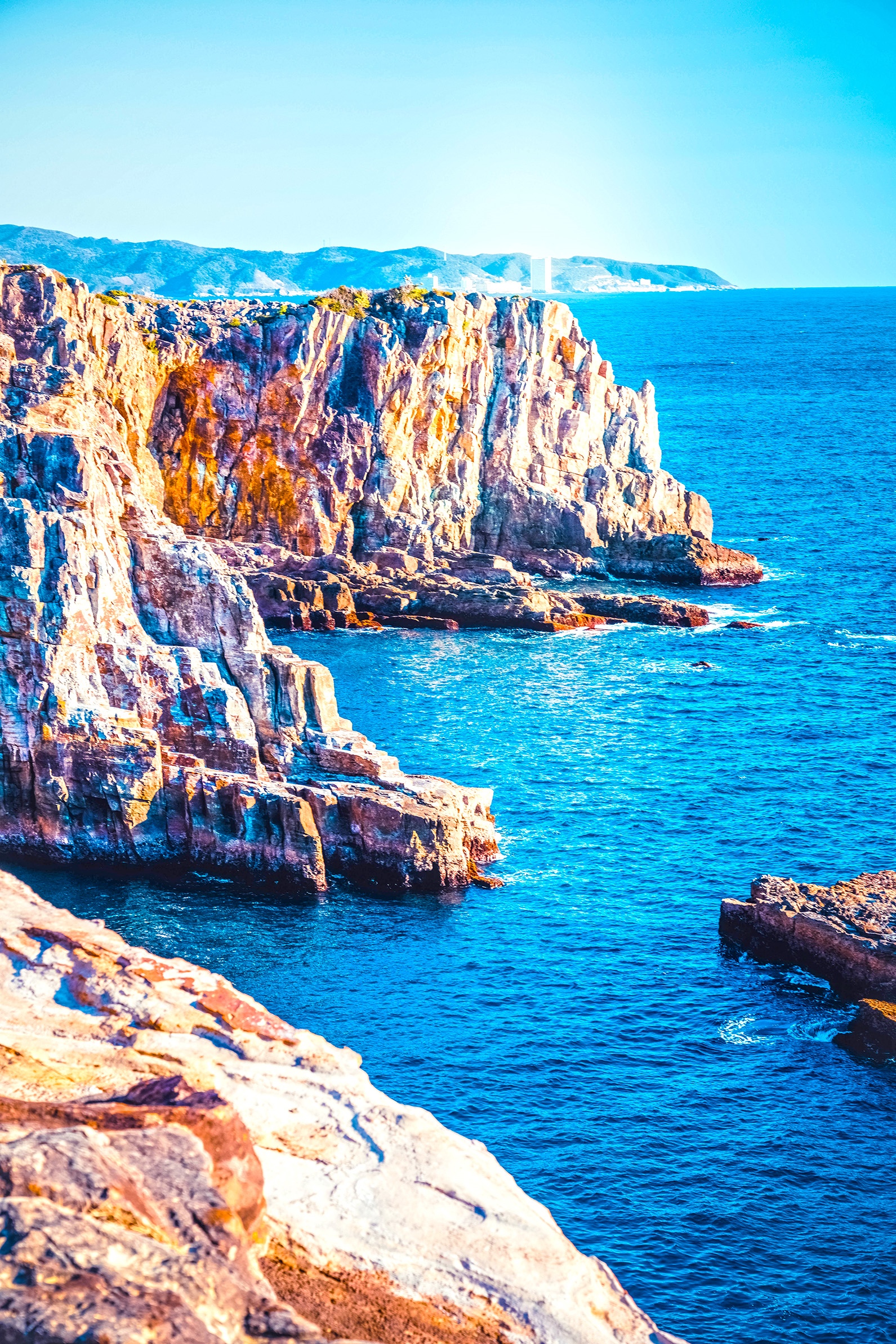 Rocky coast overlooking a bright blue sea HD Phone Wallpaper