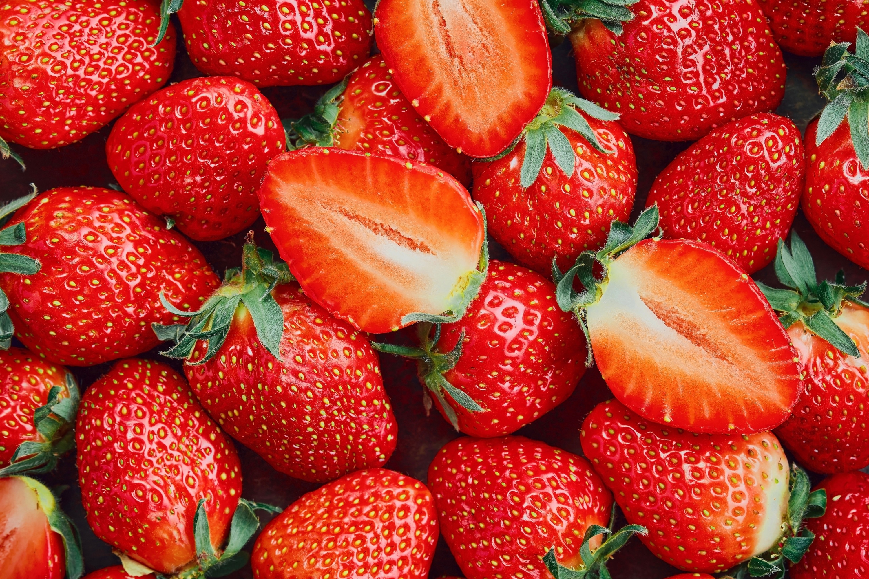 A pile of fresh strawberries, some sliced in half HD Wallpaper