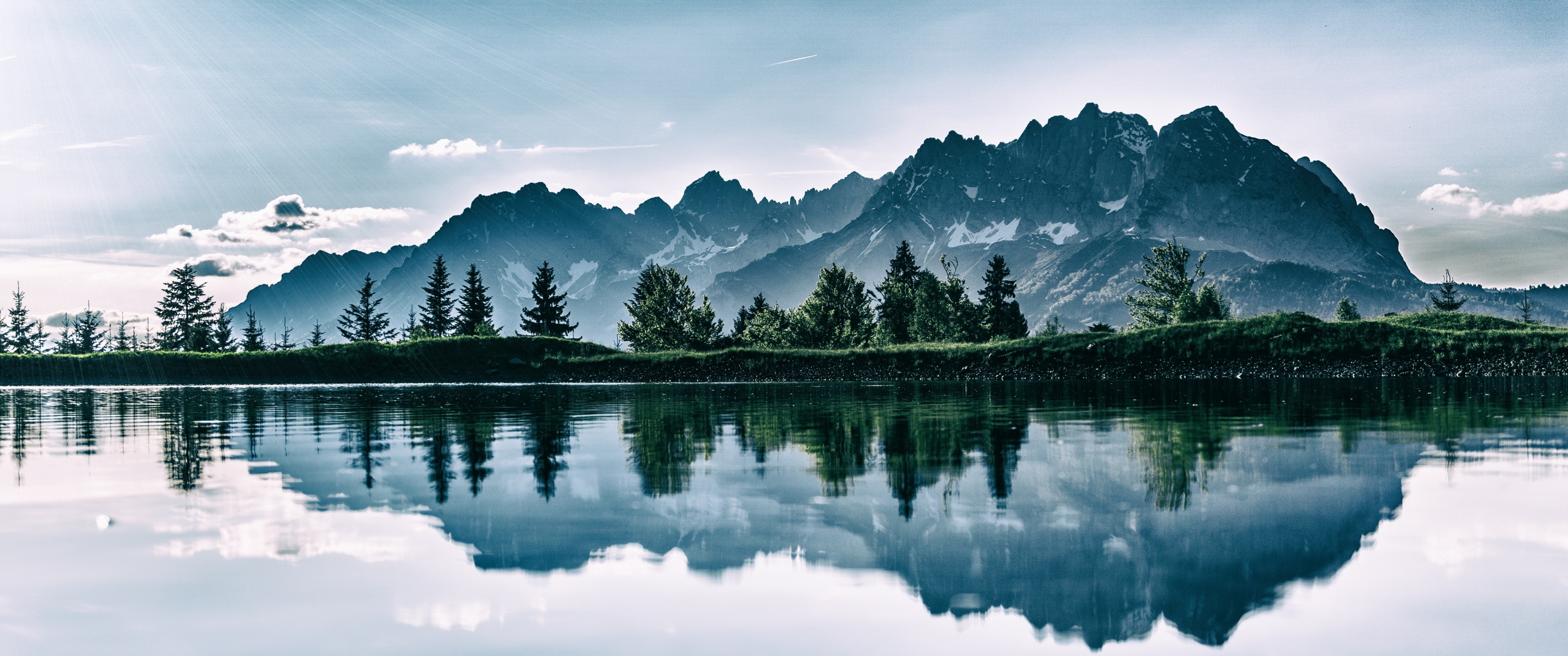 Mountain range reflected in a calm lake with pine trees HD Wallpaper