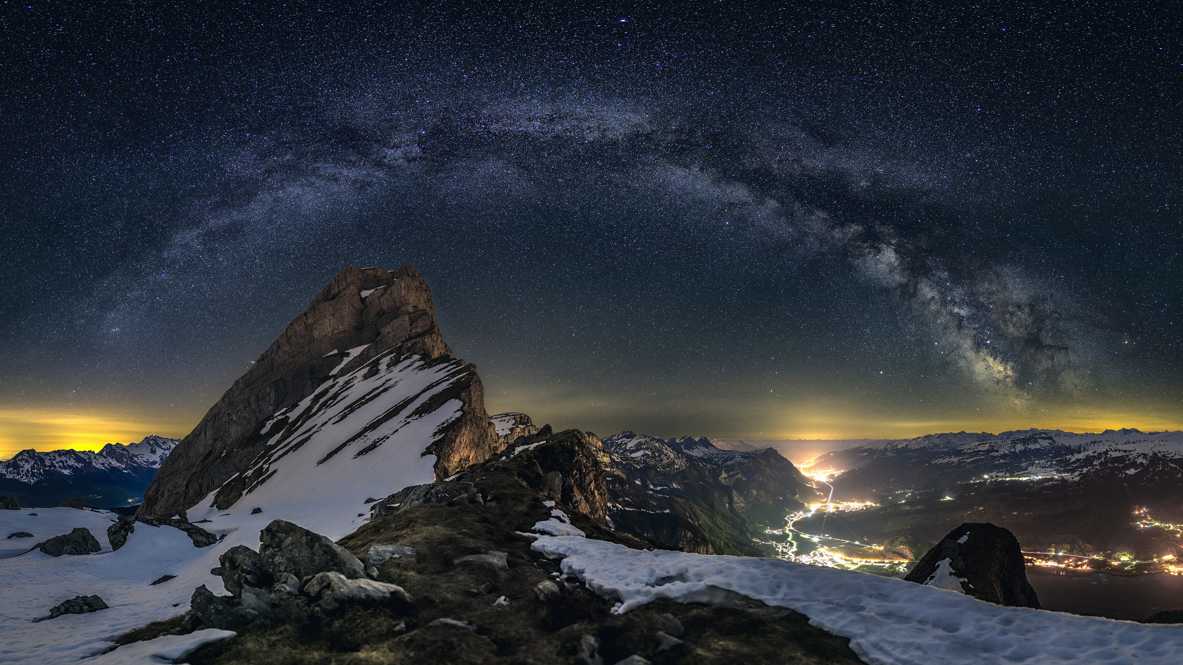 Milky Way over snowy mountains and a lit valley HD Wallpaper