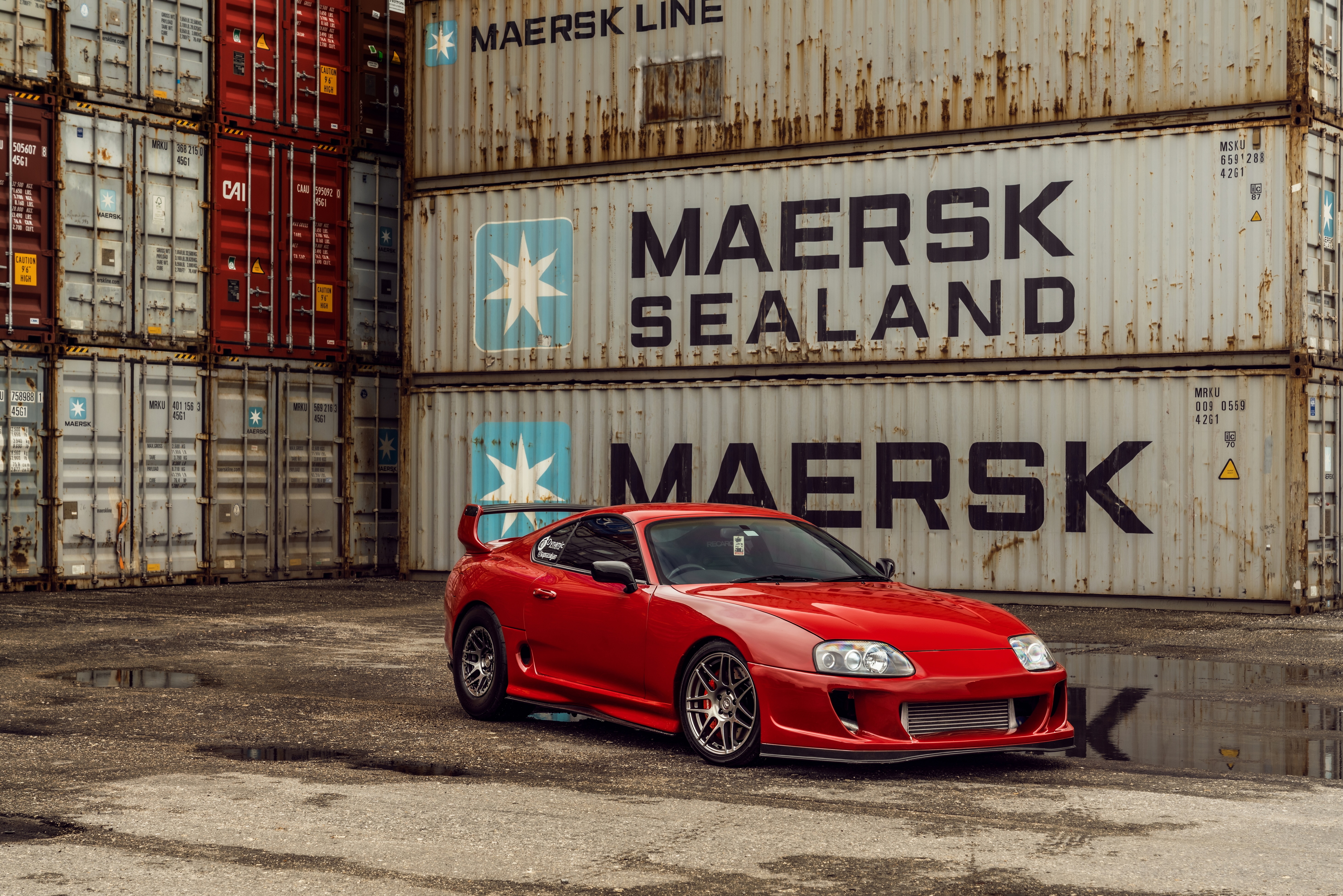 Red Toyota Supra parked near shipping containers HD Wallpaper