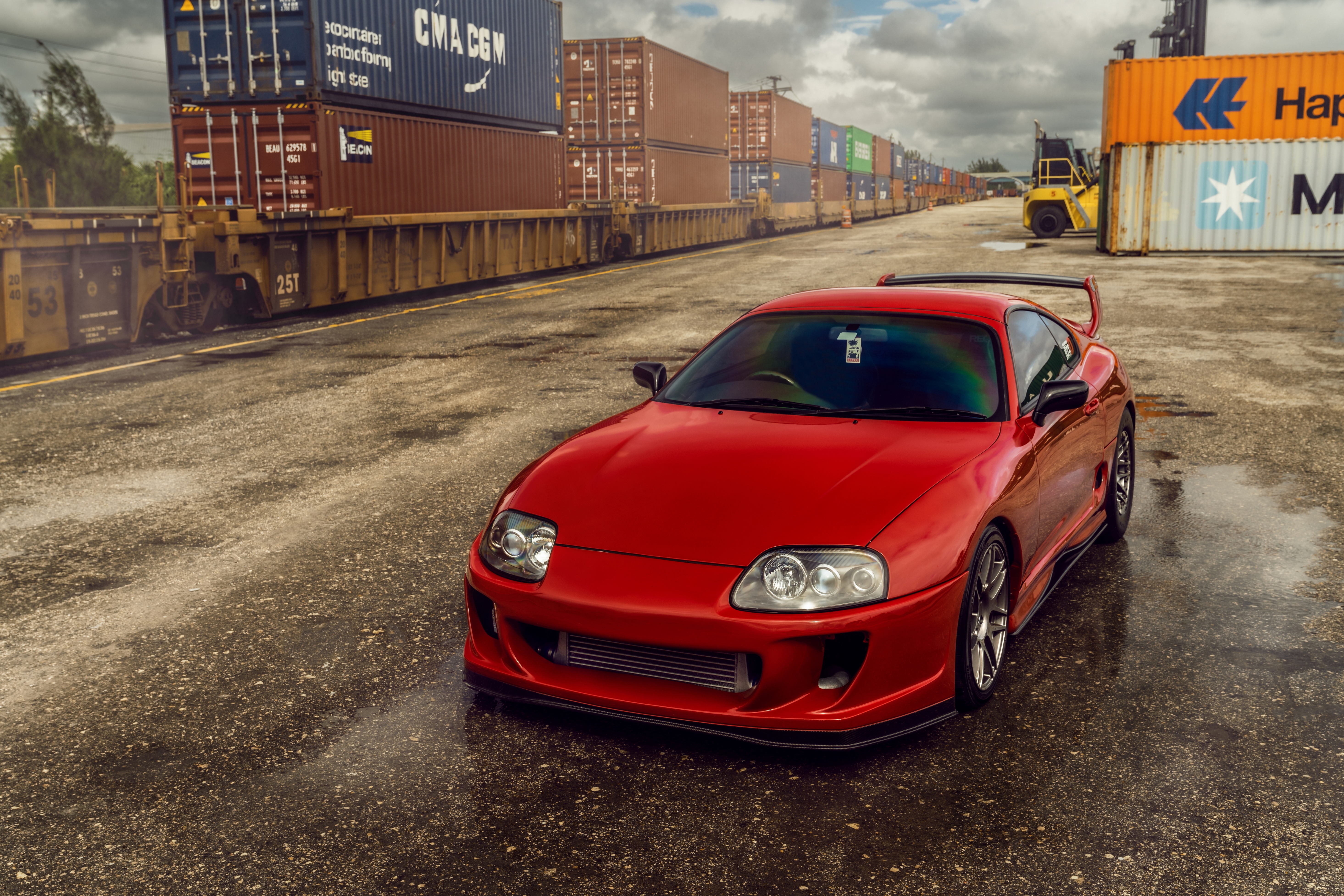 Red Toyota Supra parked near shipping containers and train HD Wallpaper