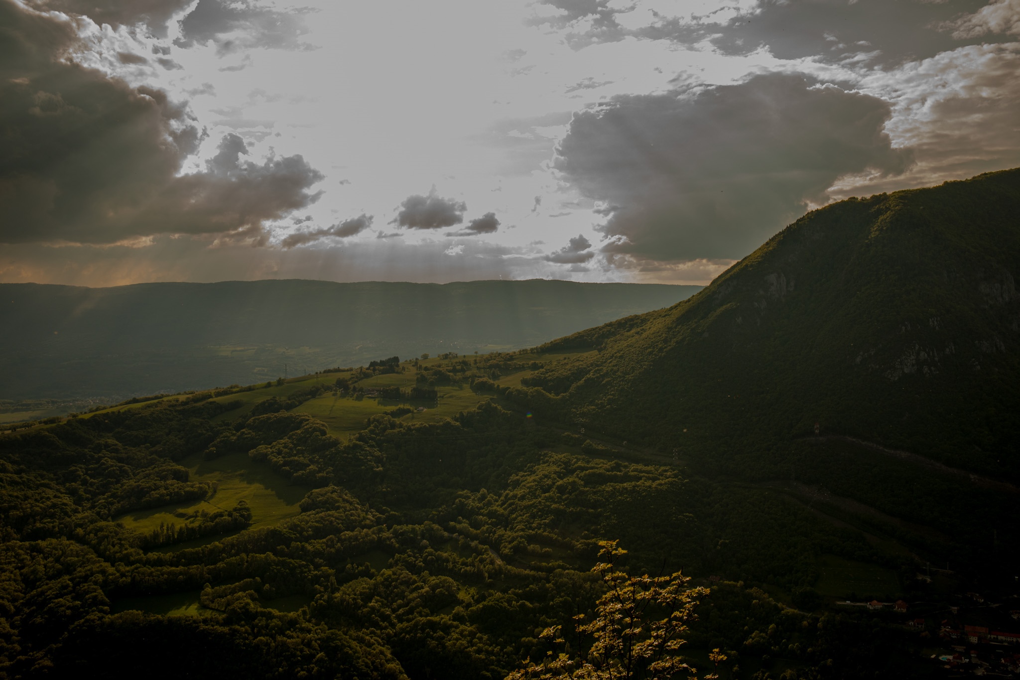 Sunlight filtering through clouds over green mountains and a village HD Wallpaper