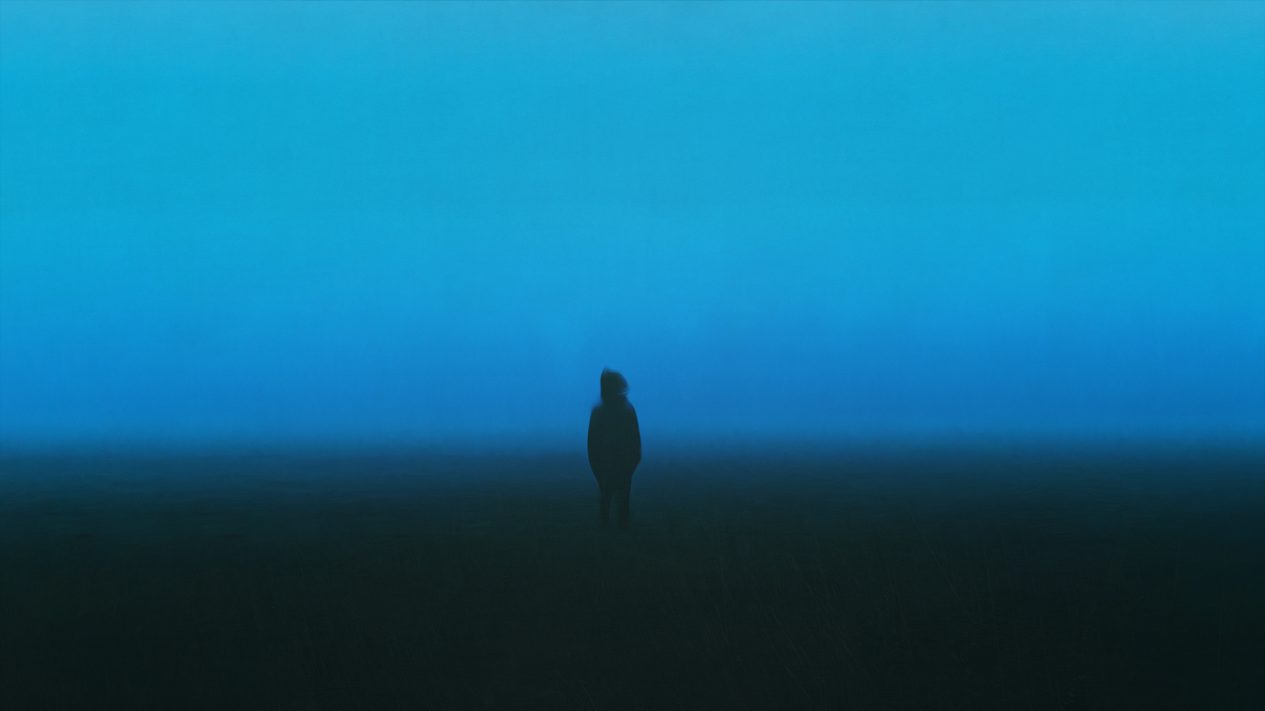 A lone figure stands in a dark, foggy landscape under a blue sky. HD Wallpaper