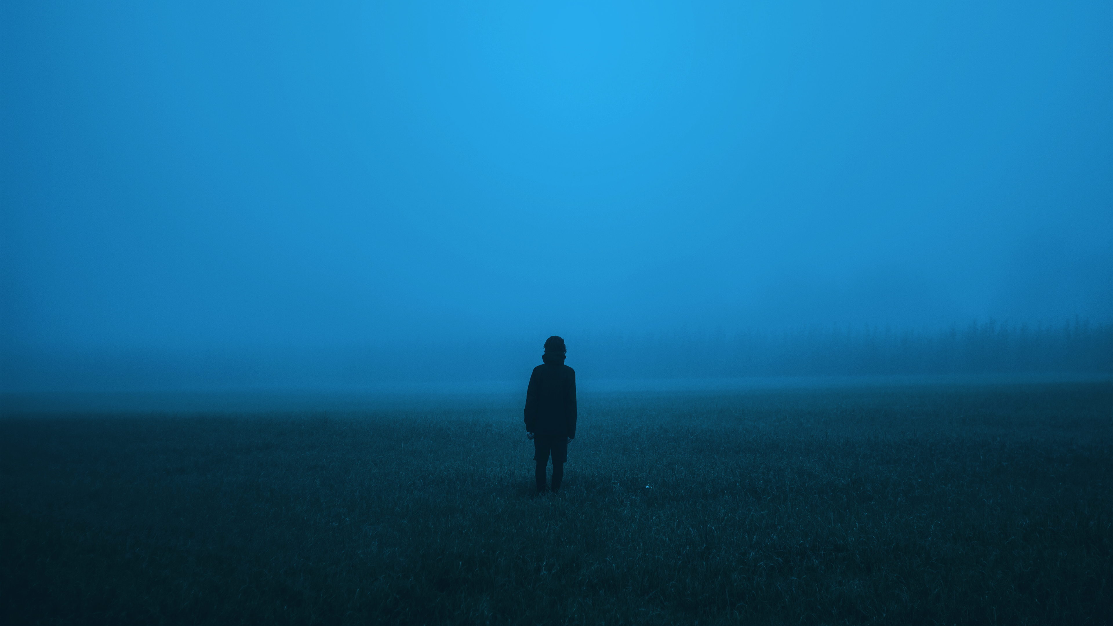 Person standing alone in a foggy field at night HD Wallpaper