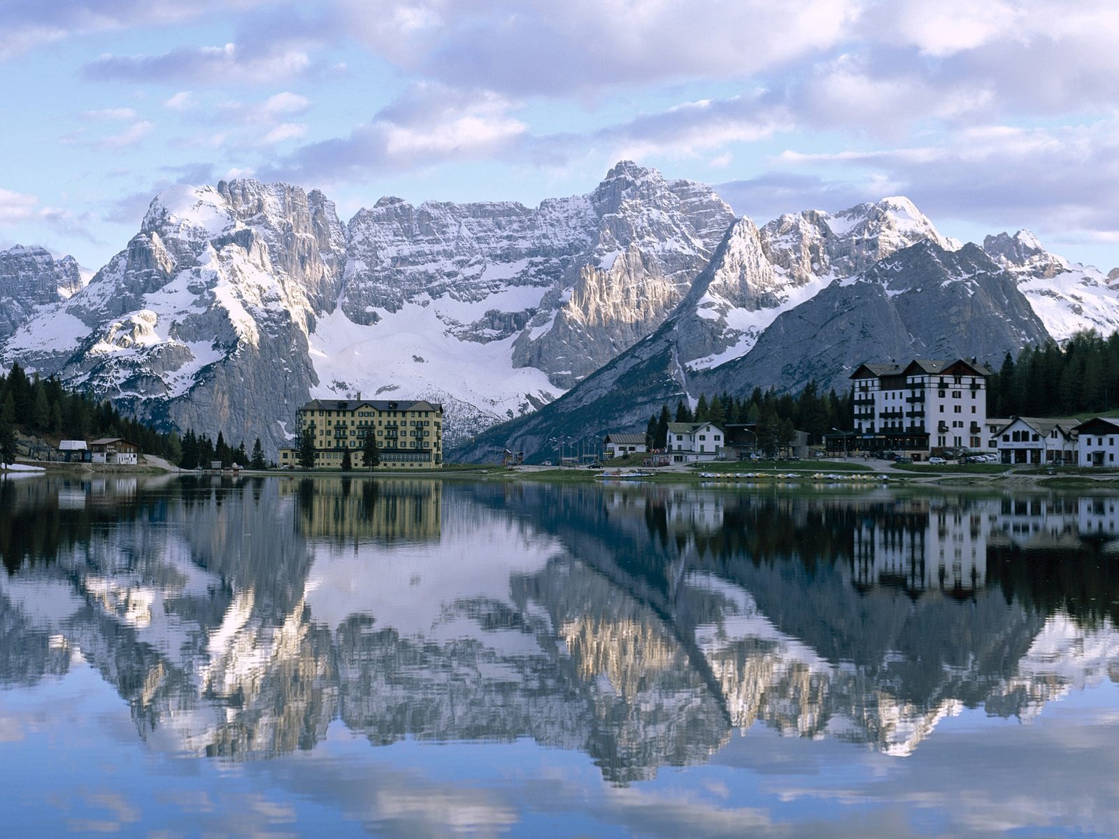 Snow-capped mountains reflected in a calm lake with hotels HD Wallpaper