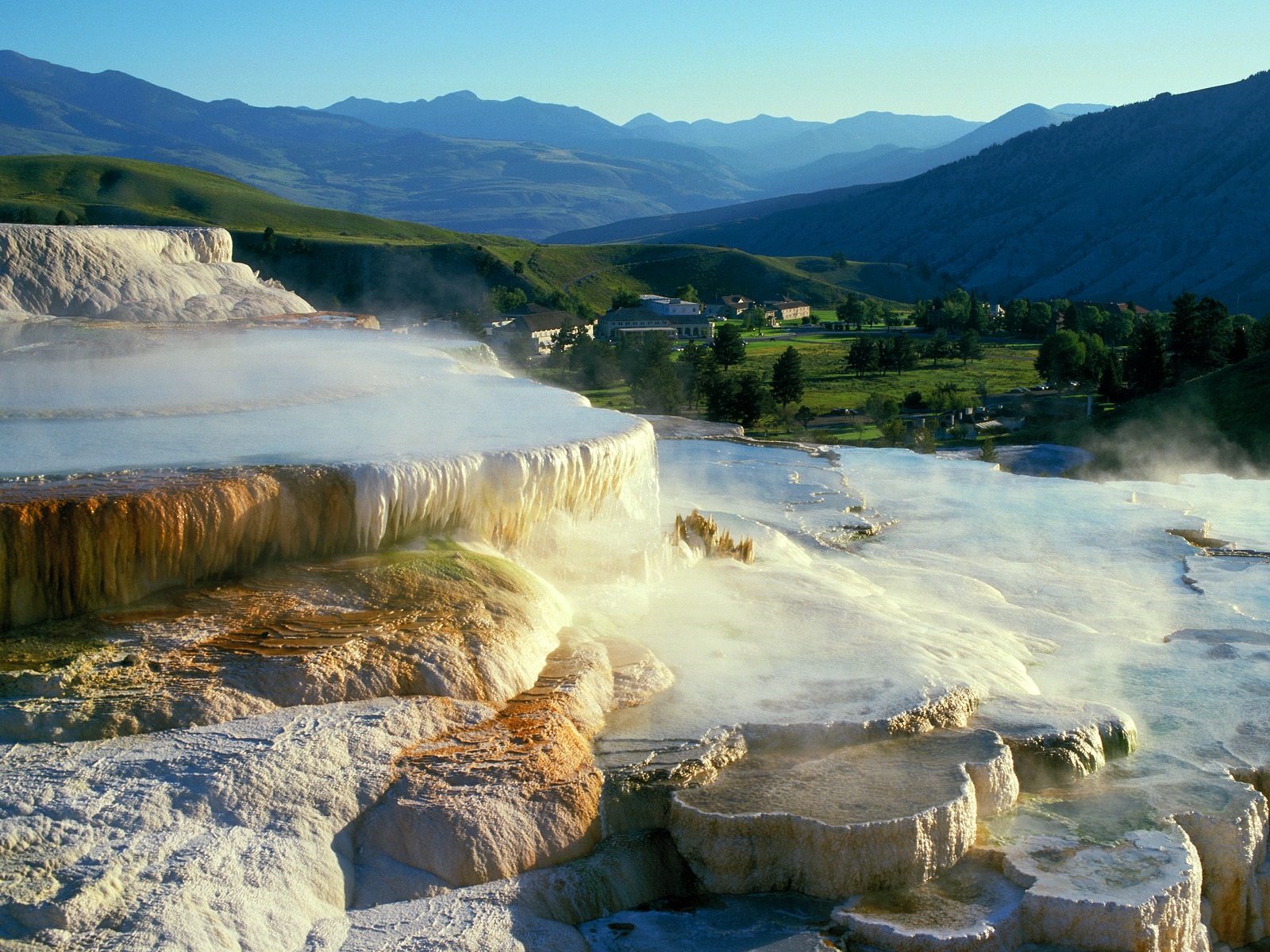 Steaming mineral terraces with mountains in the background HD Wallpaper