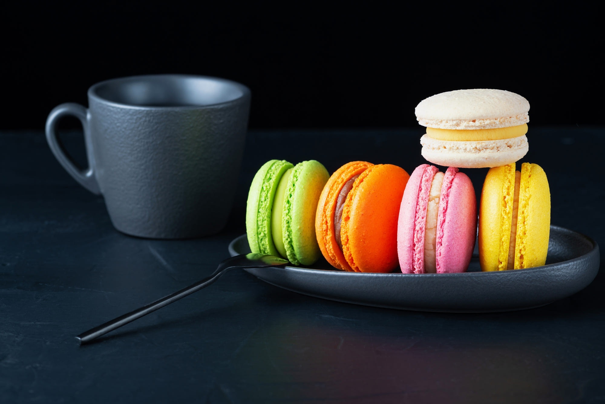 Colorful macarons and a cup of coffee on a dark surface HD Wallpaper
