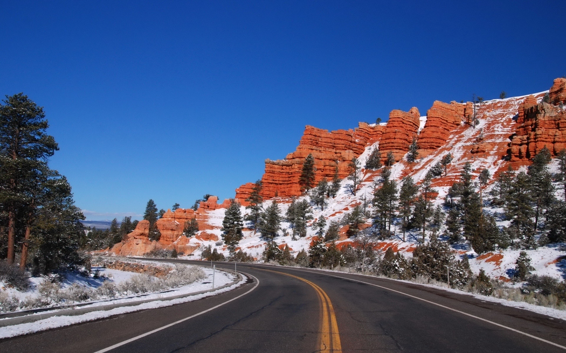 Winding road through snowy red rock formations and pine trees HD Wallpaper