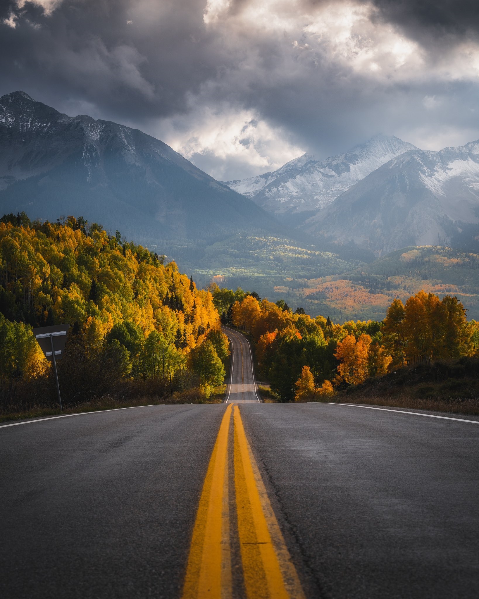 Mountain road through autumn trees under stormy clouds HD Phone Wallpaper