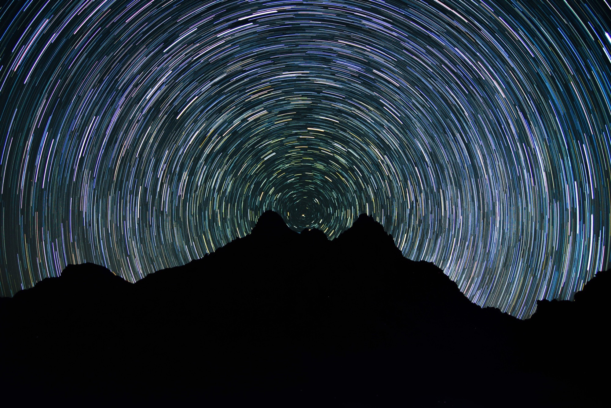 Star trails over silhouetted mountains at night HD Wallpaper