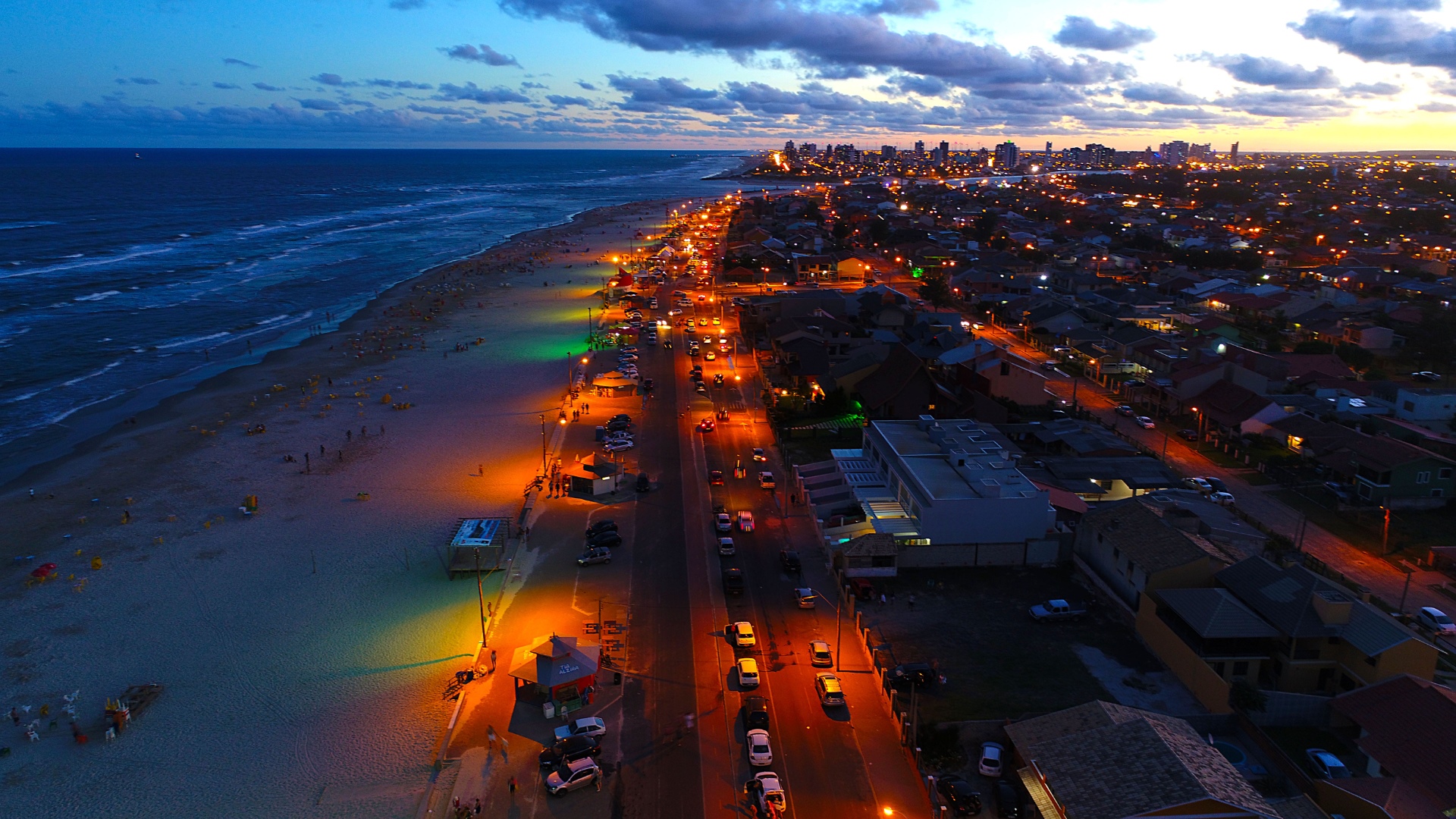Aerial view of a beach city at dusk with ocean and lights HD Wallpaper