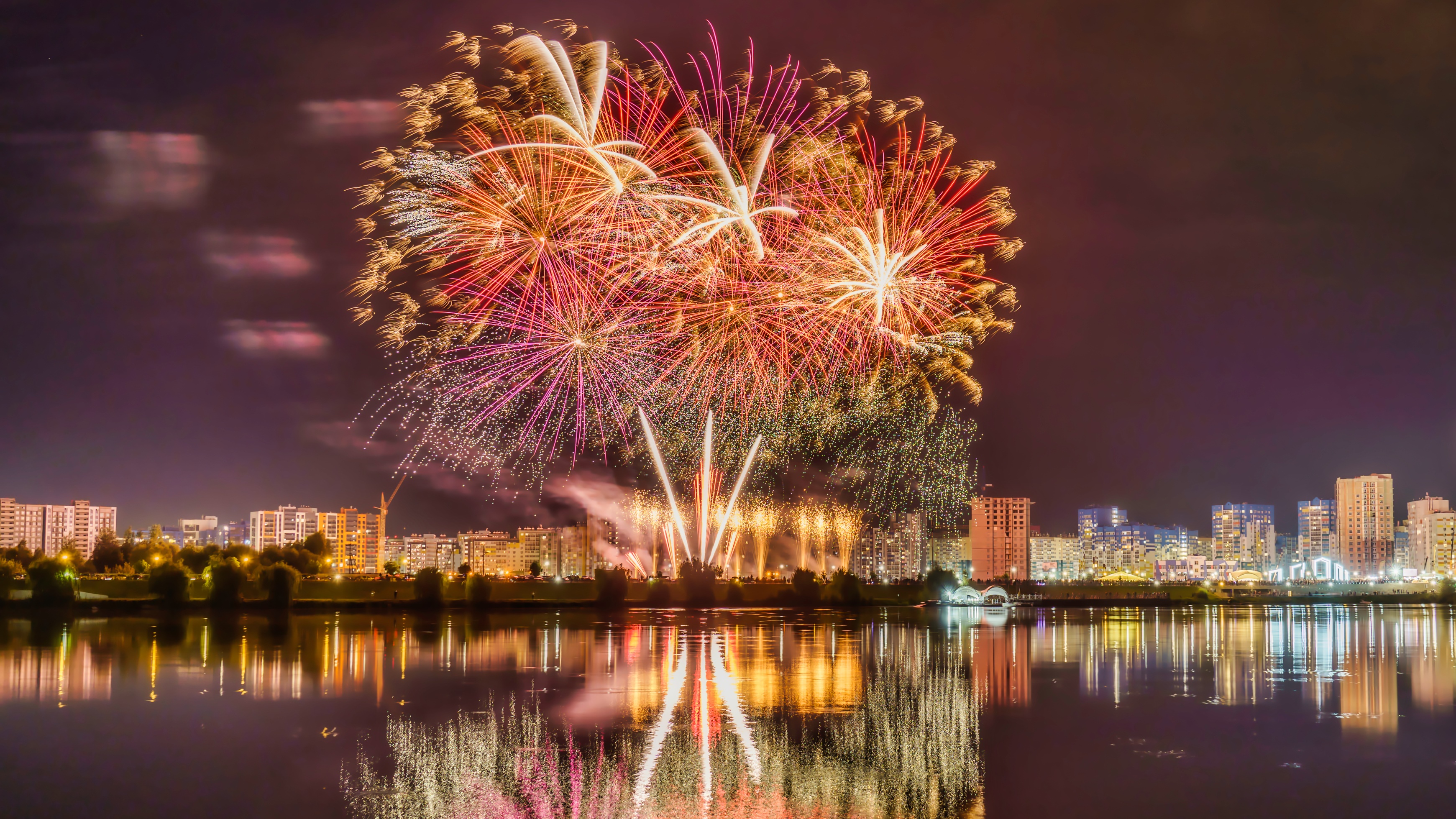 Fireworks over a city reflected in water at night HD Wallpaper