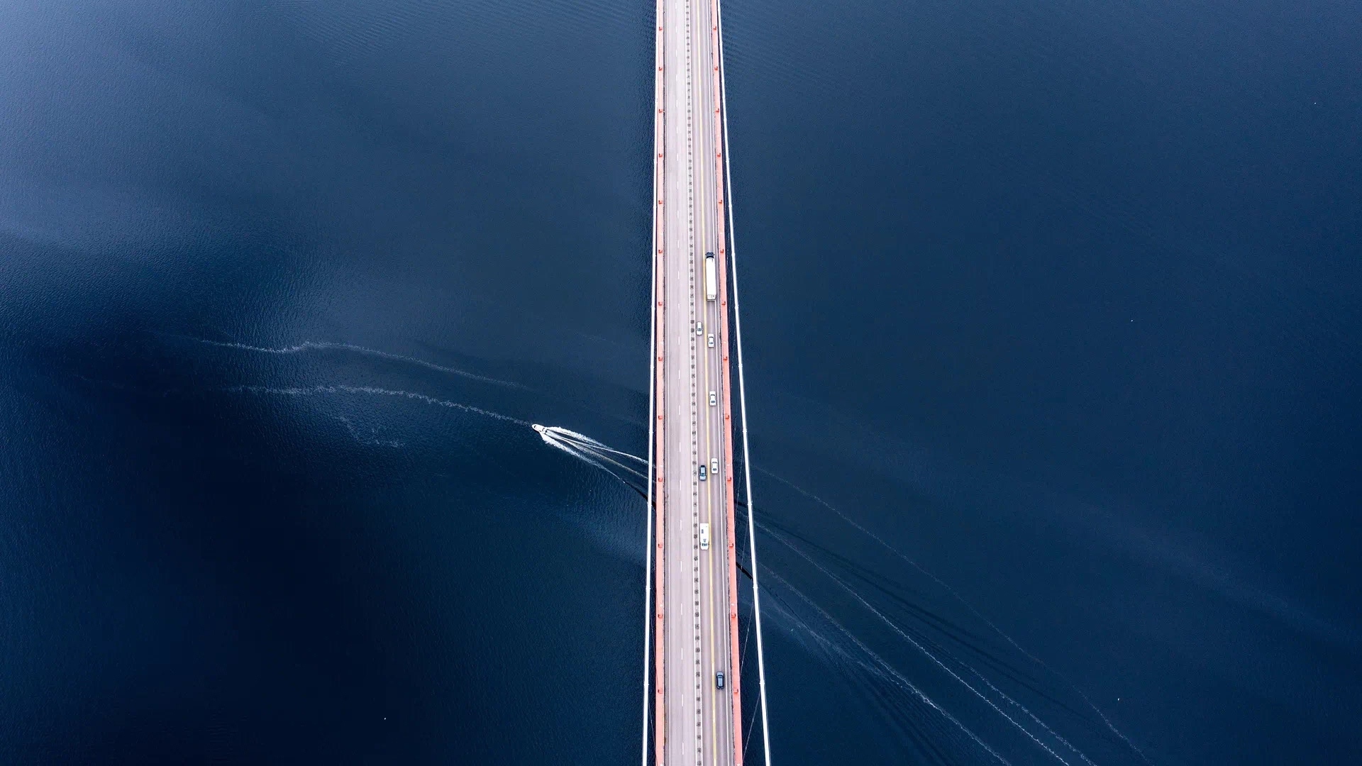 Aerial view of a bridge over a dark blue body of water with a boat HD Wallpaper