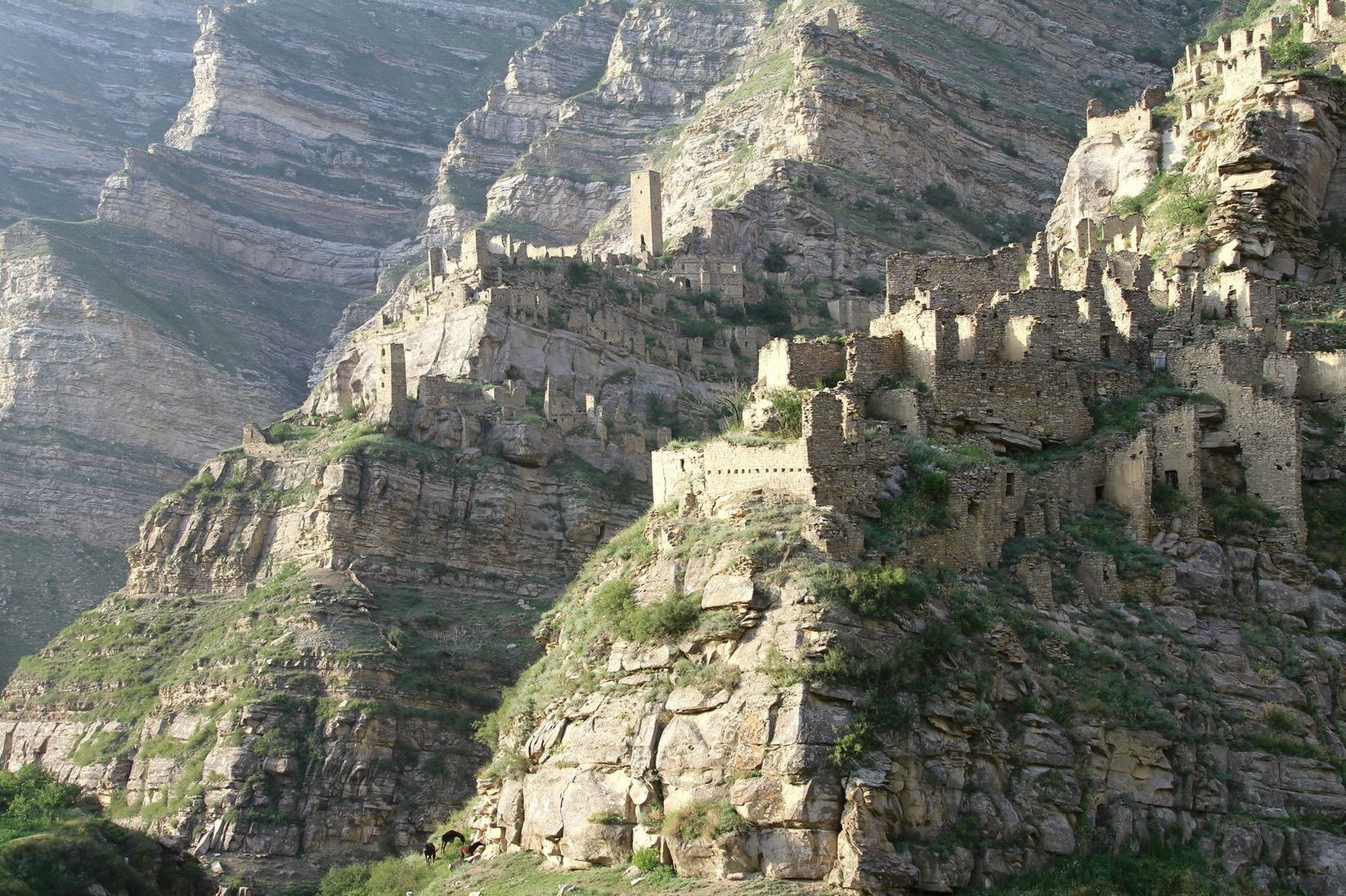 Ancient stone ruins perched on a steep mountain slope in the Caucasus HD Wallpaper
