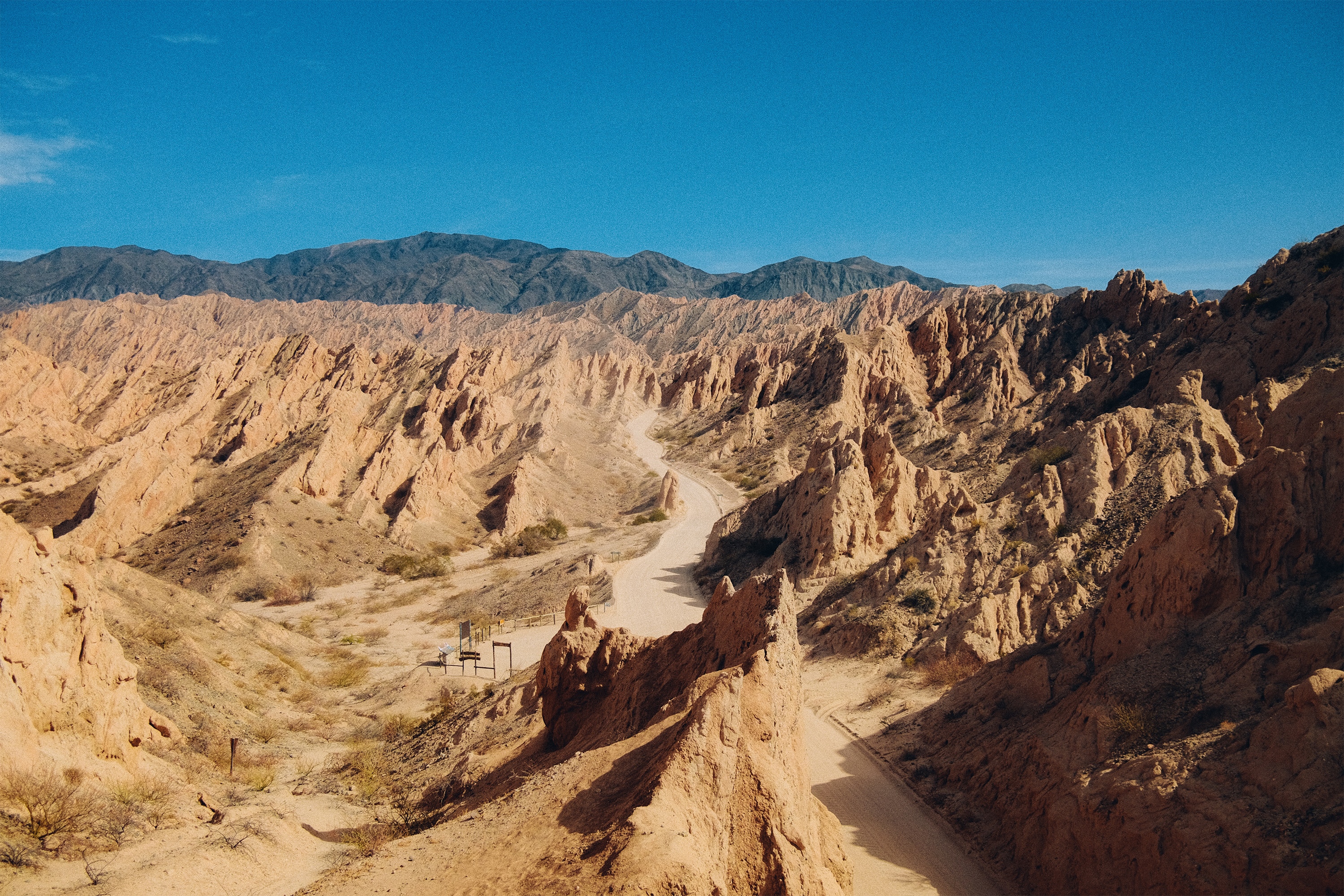 Winding dirt road through a desert canyon with mountains in the background HD Wallpaper