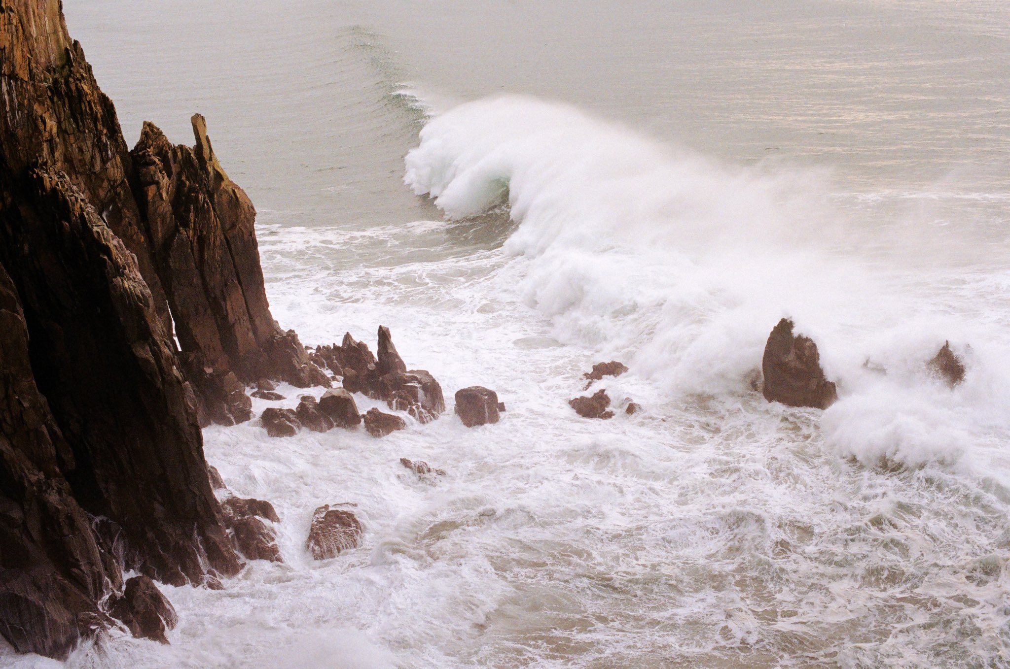 Crashing waves against rocky cliffs on a cloudy day HD Wallpaper