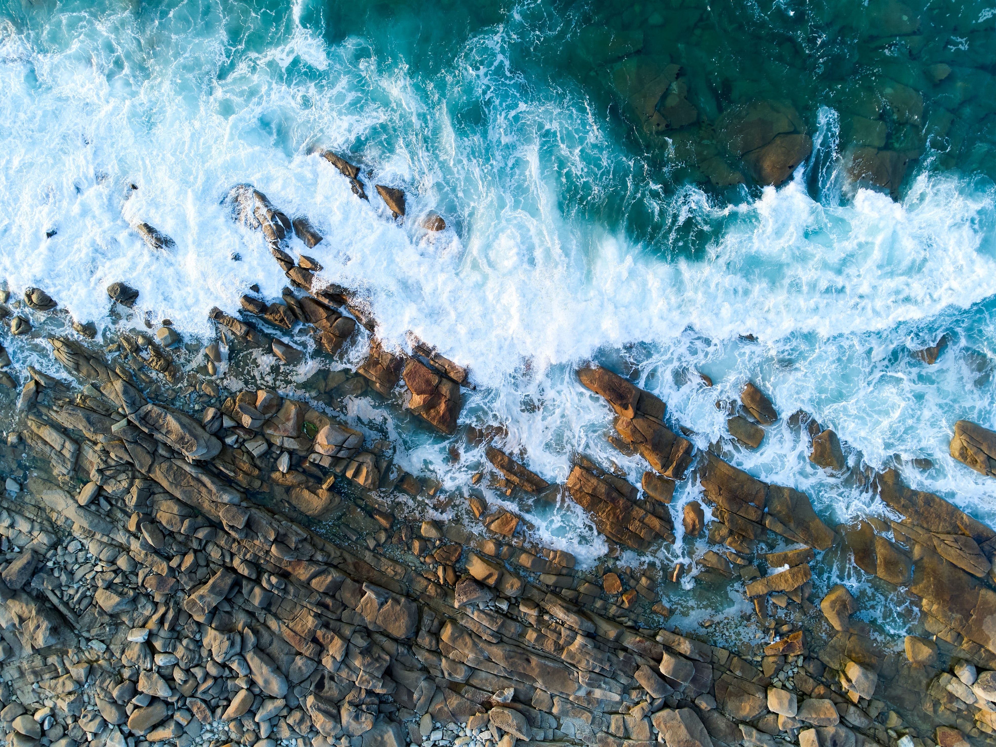 4K Aerial View of Waves Crashing on Rocky Coastline HD Wallpaper