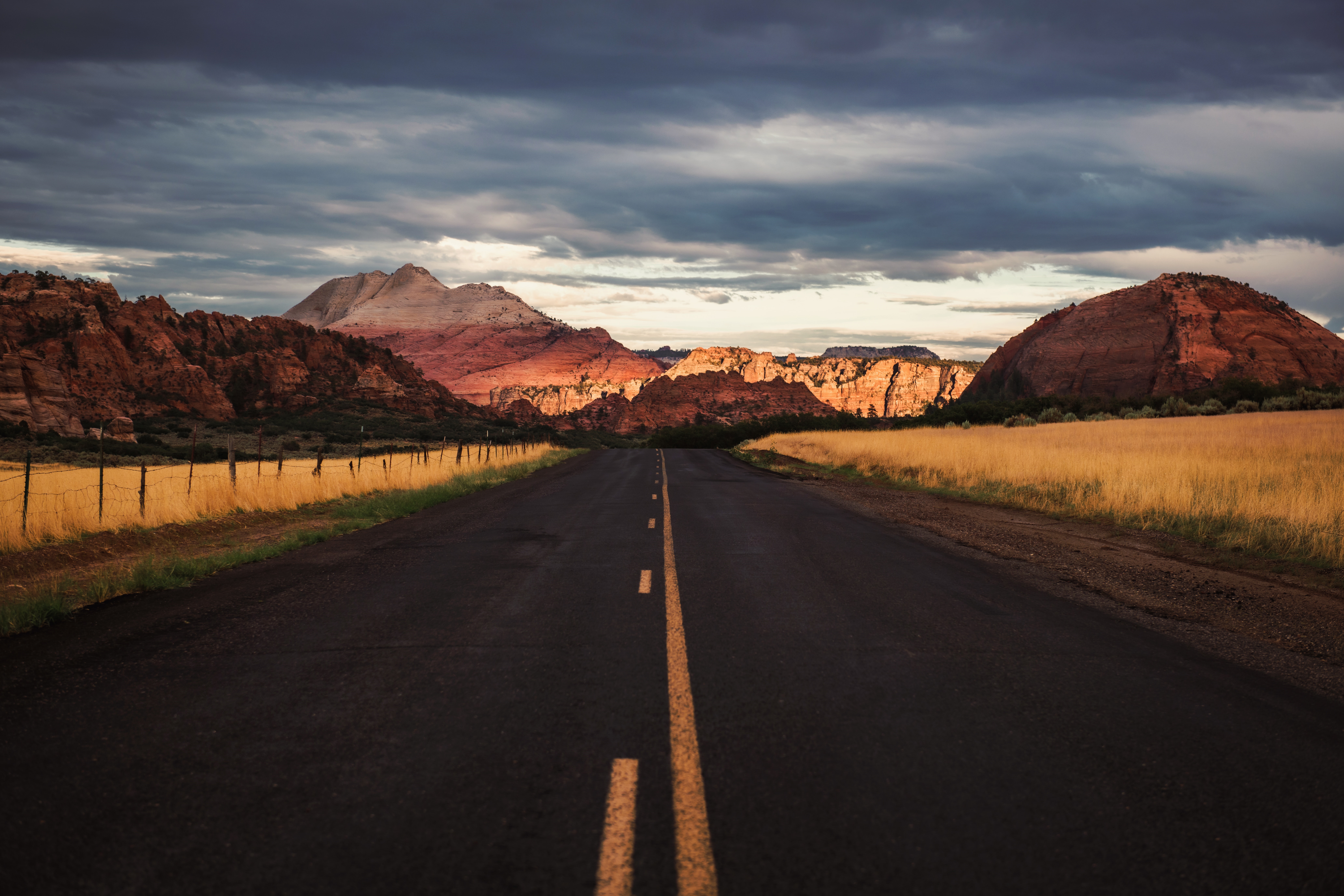 Road through rocky mountains under cloudy sky HD Wallpaper