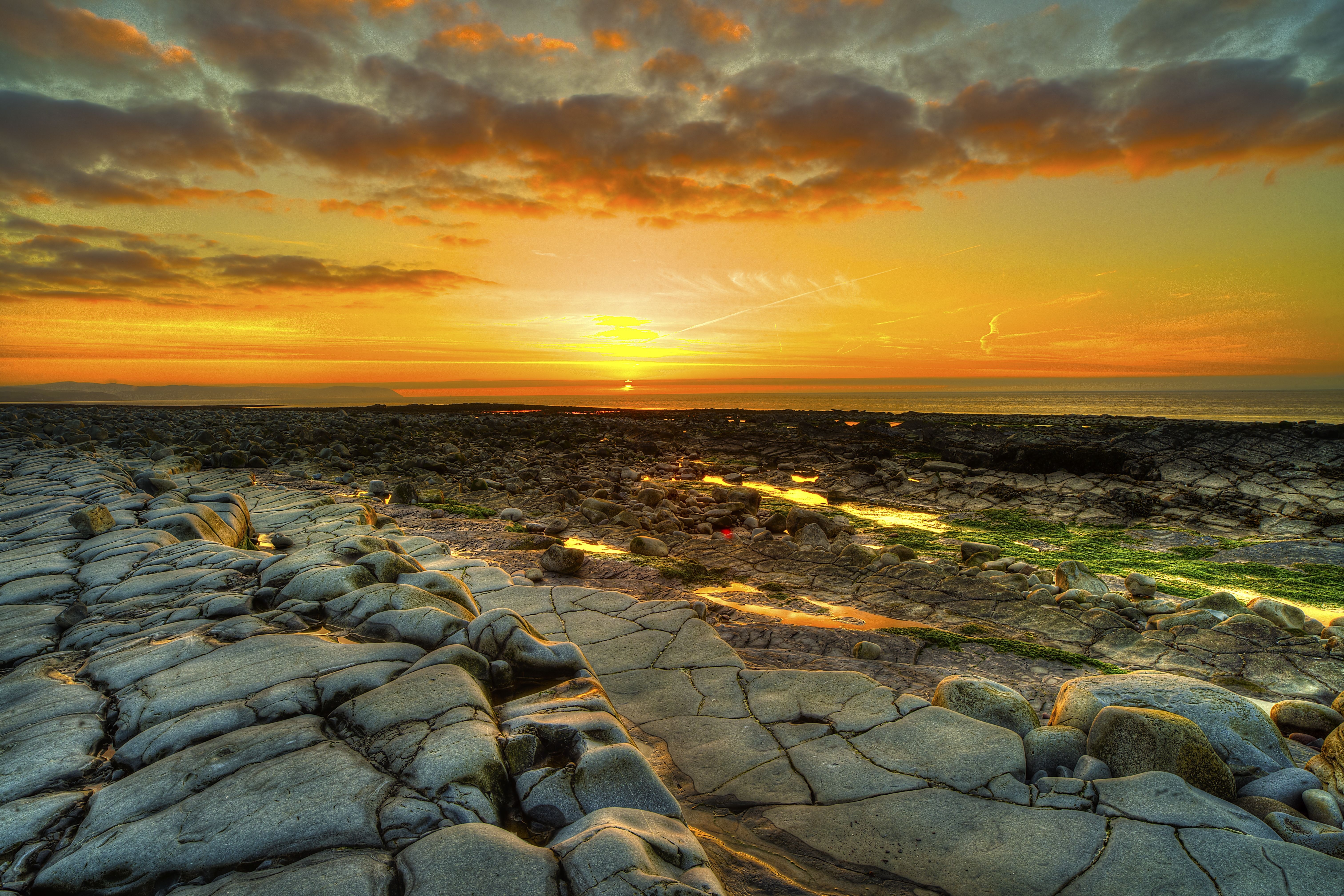 4K sunset over rocky coastline with orange clouds HD Wallpaper
