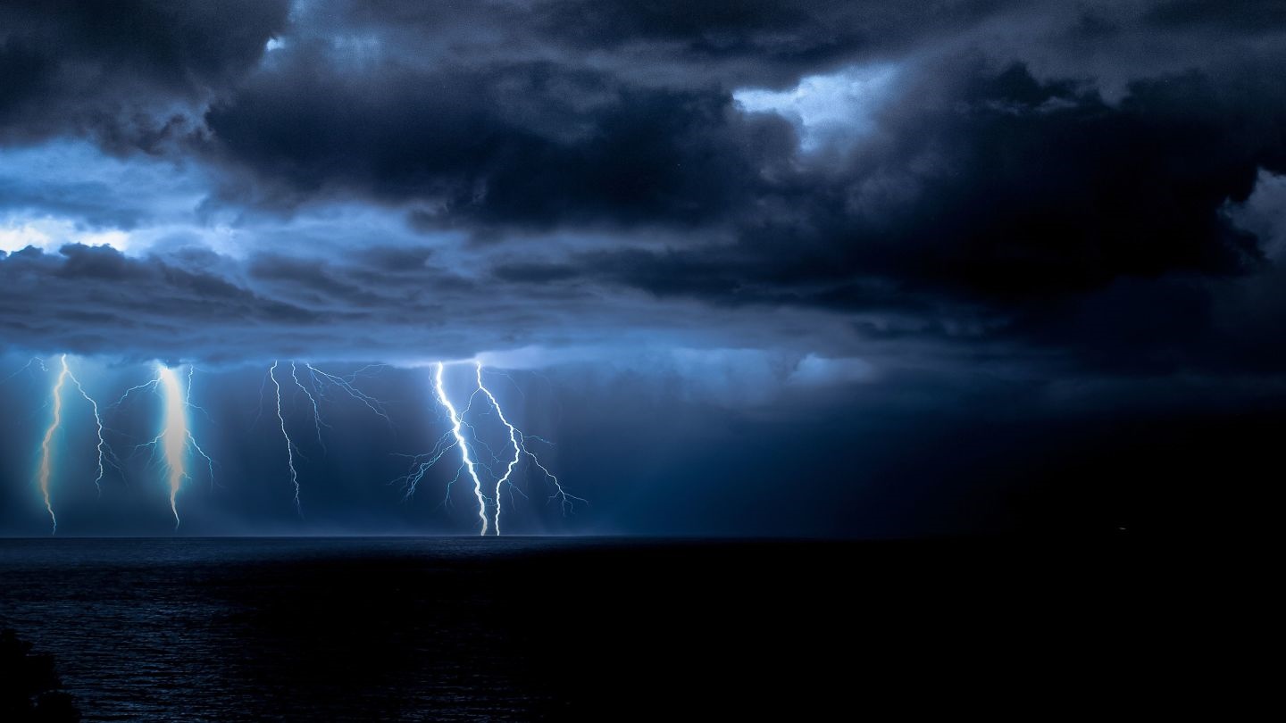 Lightning strikes over a dark ocean during a storm HD Wallpaper