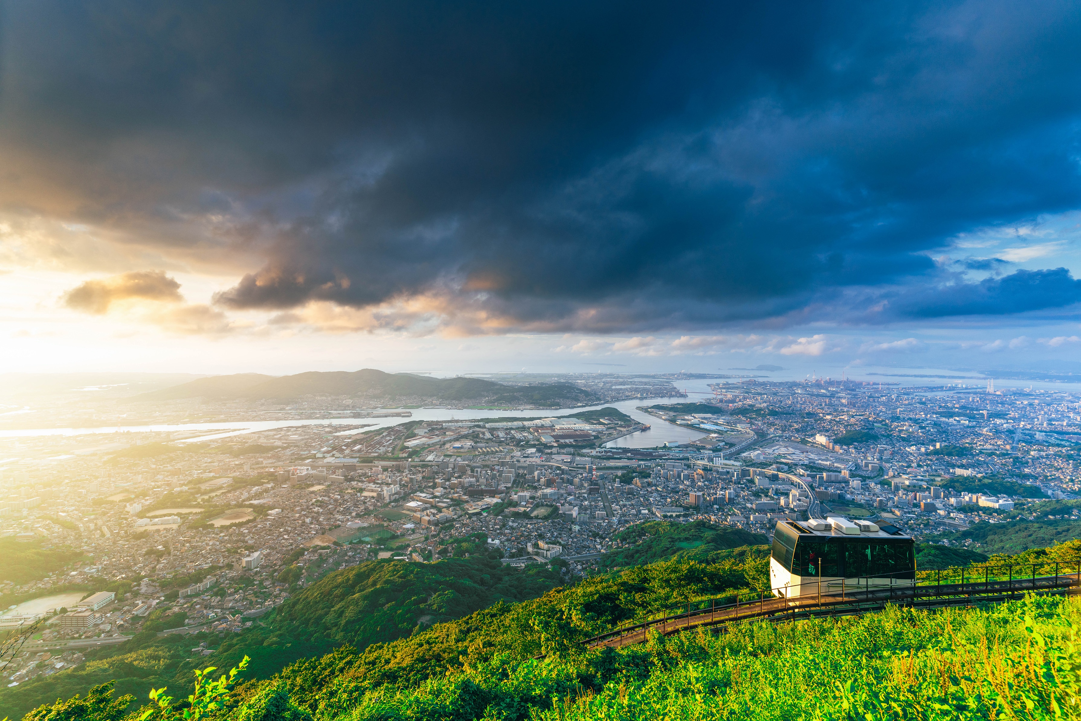 Cityscape overlooking a river and bay under dramatic clouds HD Wallpaper