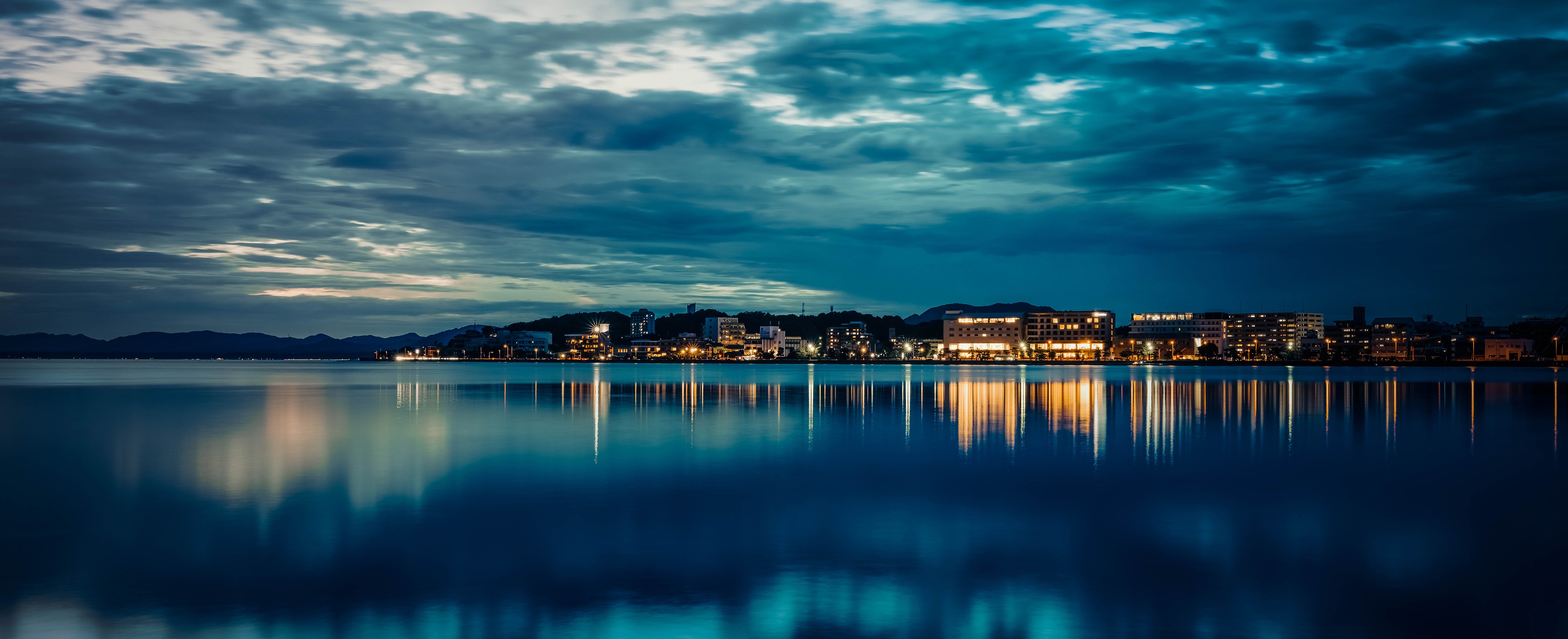 City lights reflected on water at dusk HD Wallpaper