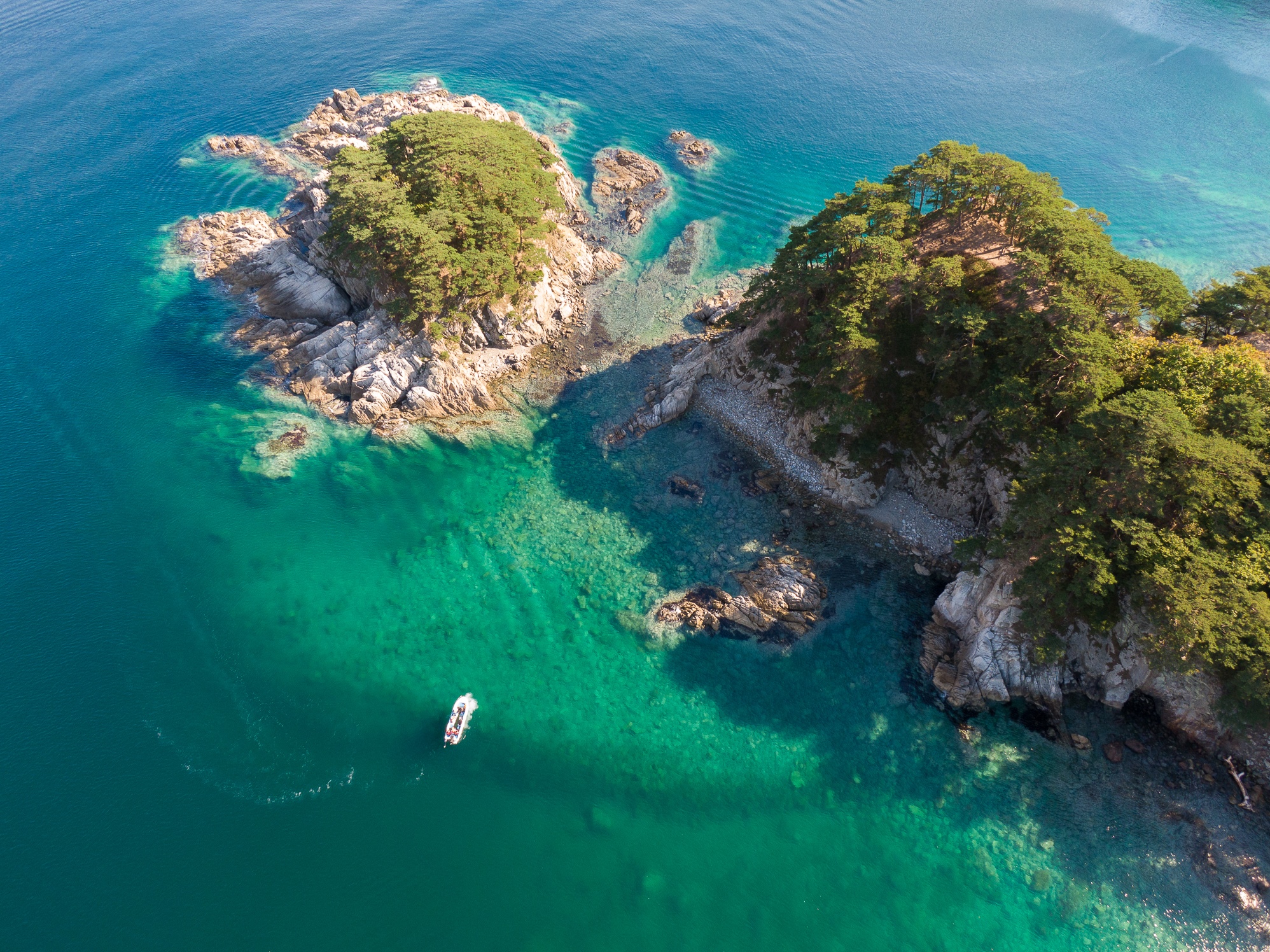 Aerial view of a small boat near rocky islands covered in trees HD Wallpaper