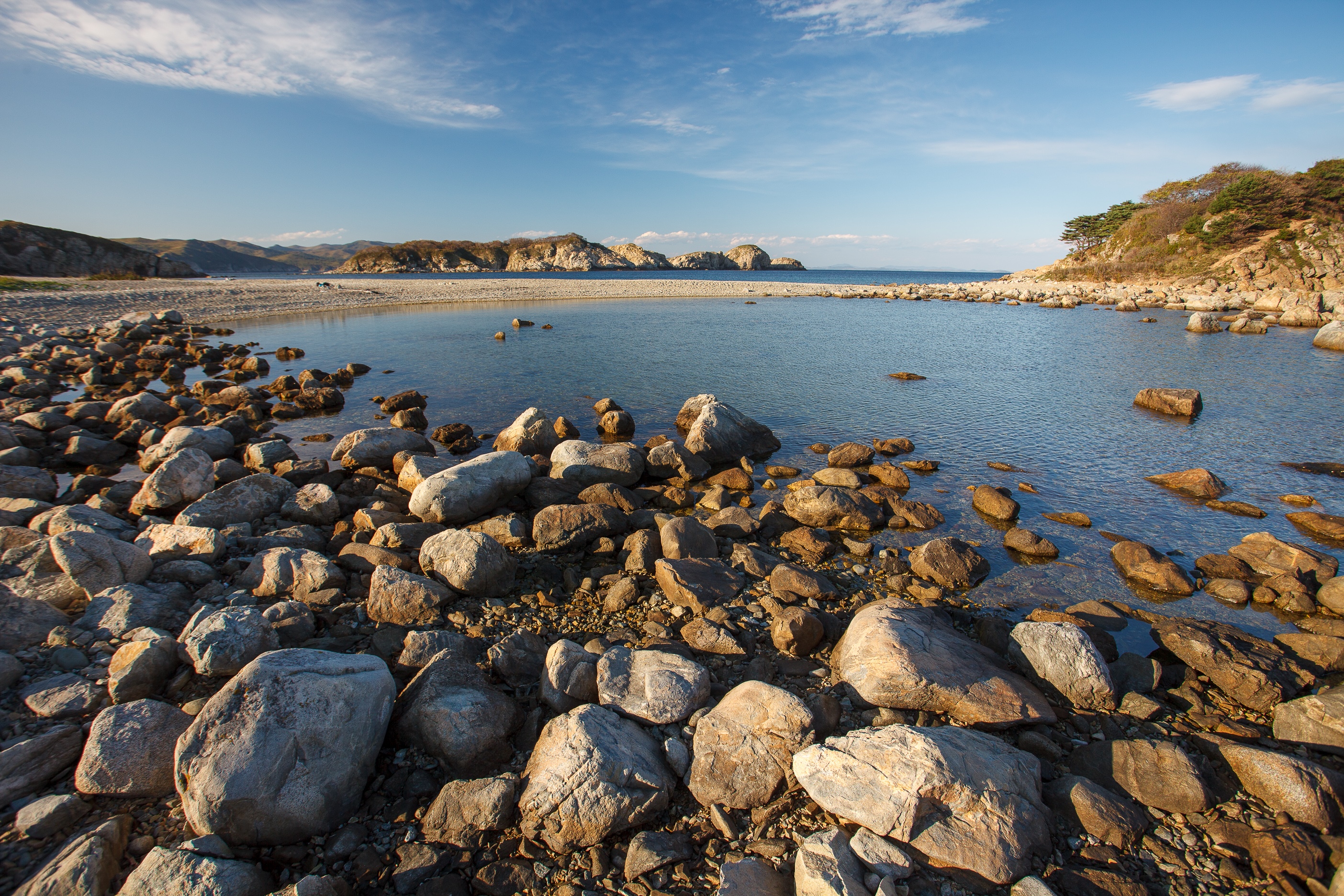 Rocky coastline with calm water and distant hills HD Wallpaper